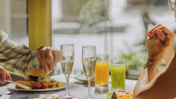 A dining table with plates of food, glasses of beverages, and a person holding hands.