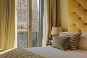 Een hotelkamer met een groot bed, een nachtkastje met een lamp en uitzicht op een gebouw door het raam.