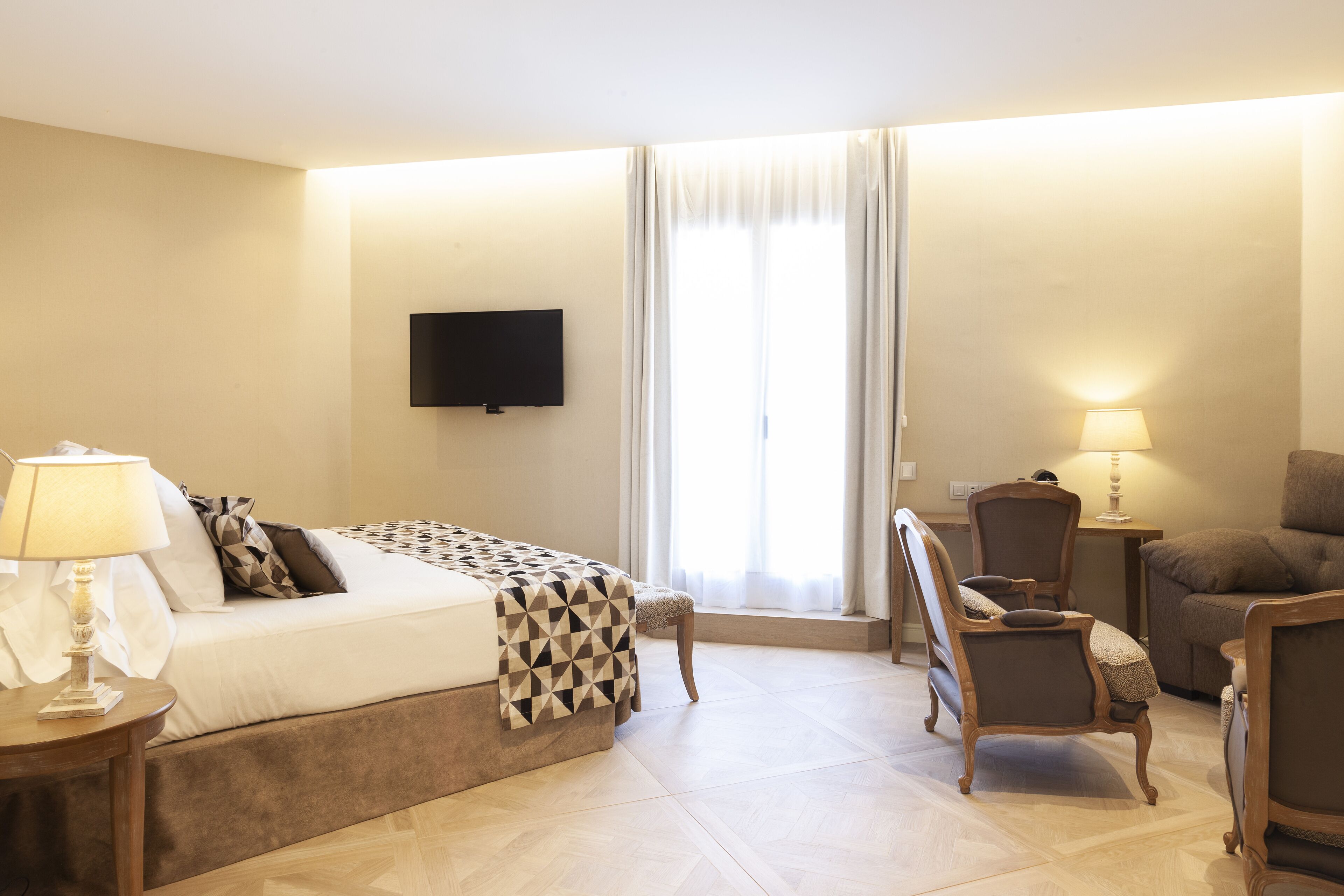Une chambre d’hôtel avec un lit, un téléviseur fixé au mur, une chaise, une table et une lampe.