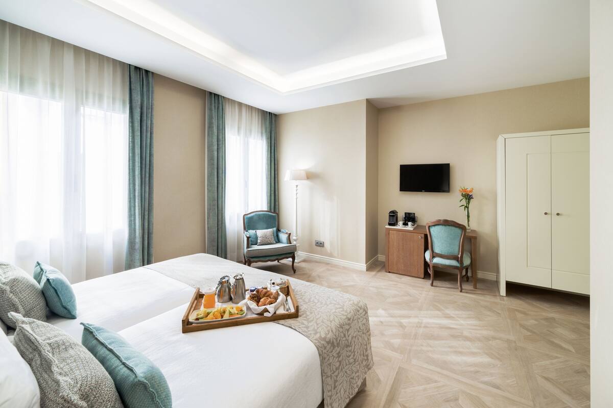 Quarto de hotel com uma cama grande, duas poltronas, uma escrivaninha e um guarda-roupa.