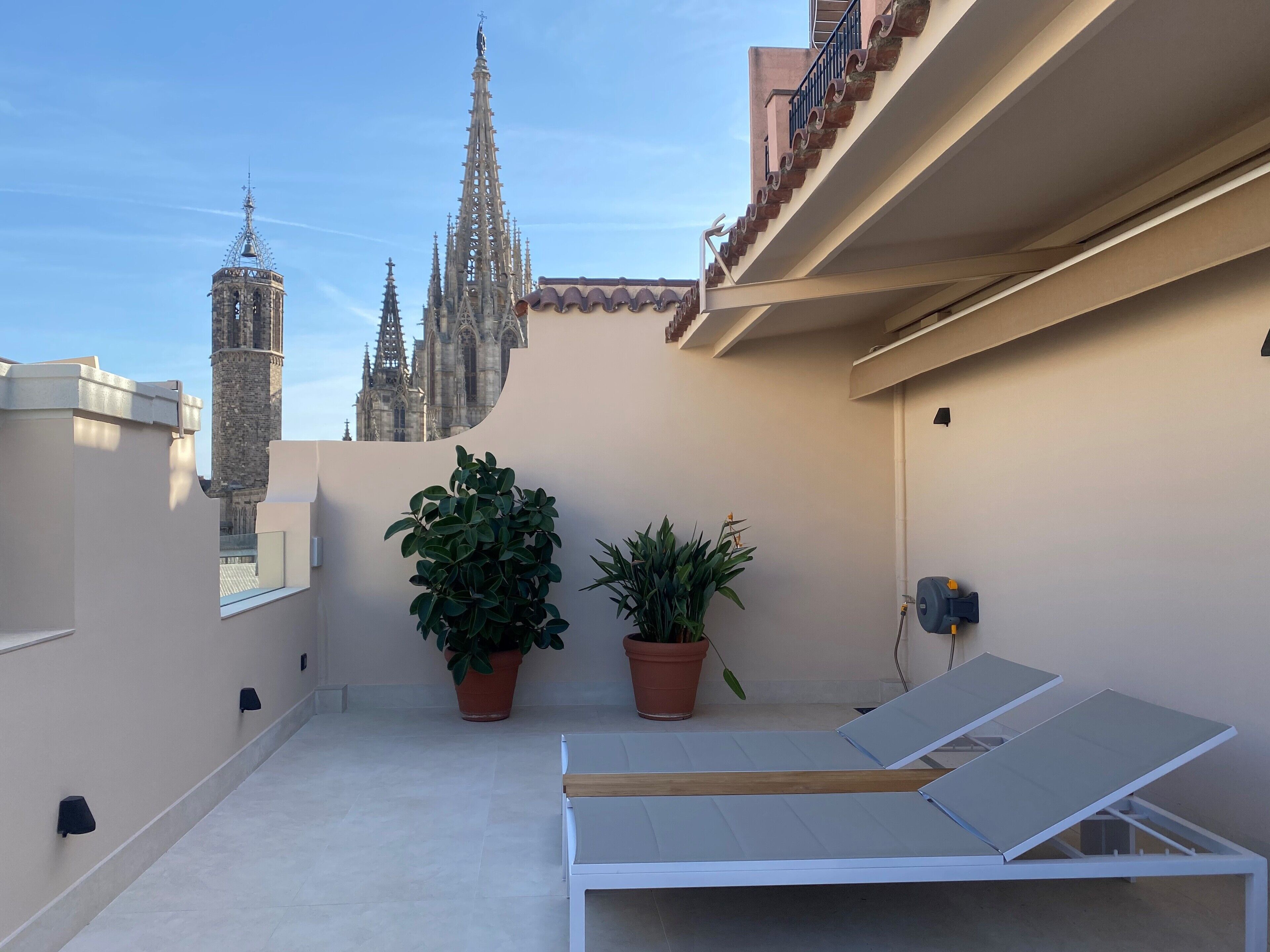 A rooftop terrace with a white lounge chair, two potted plants, and a view of a historic cathedral.
