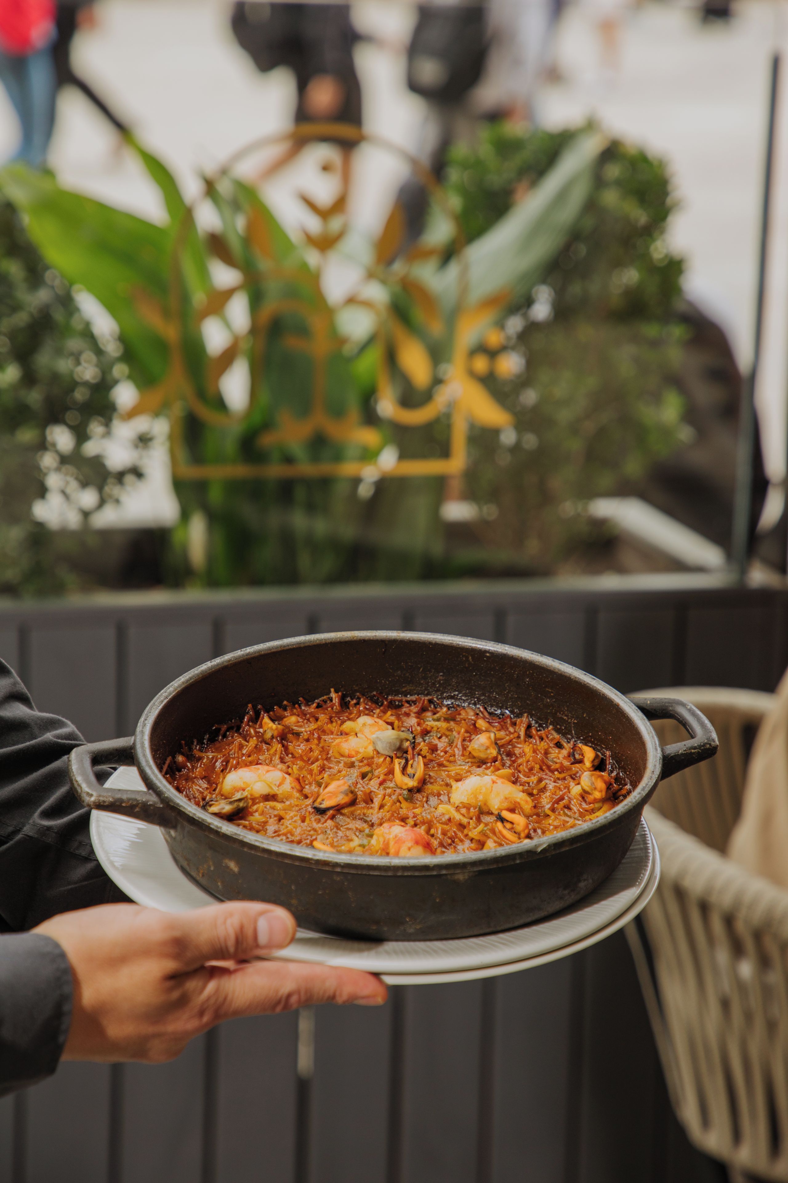 A person holding a large pot of food, possibly a stew or curry, with a metal handle and a lid.