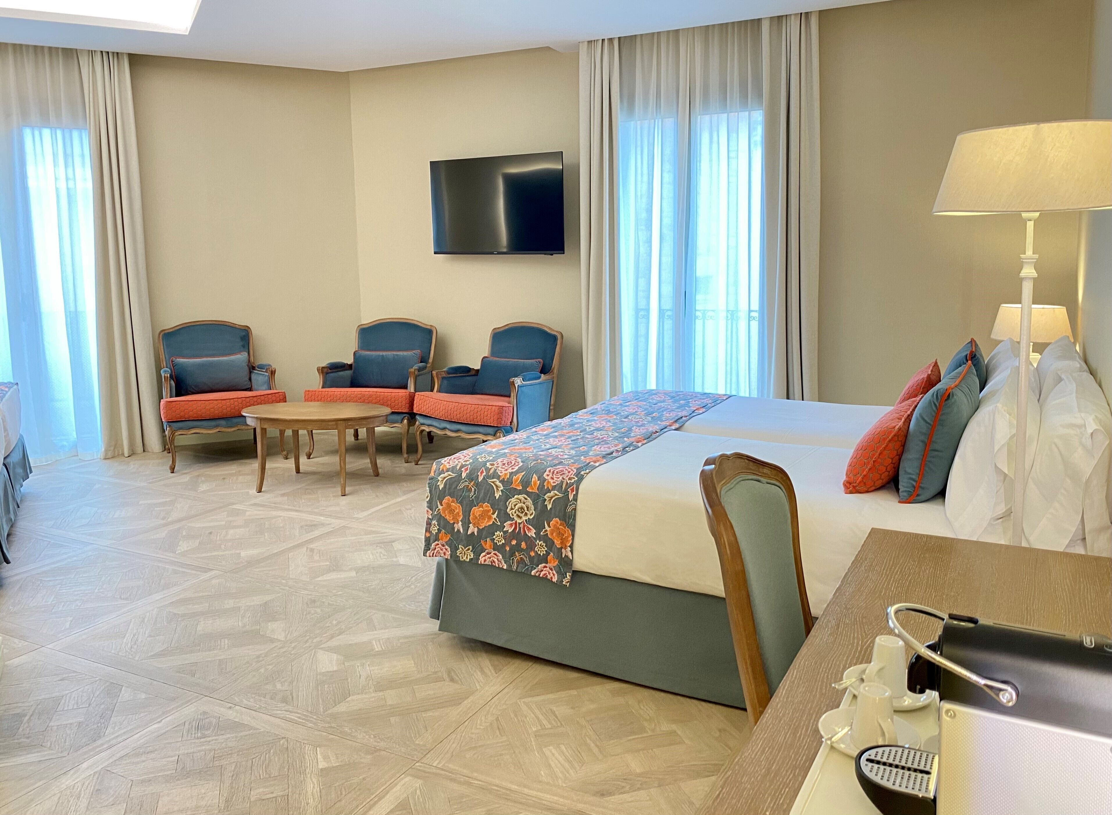 A hotel room with a bed, two armchairs, a small table, a TV, and a lamp.