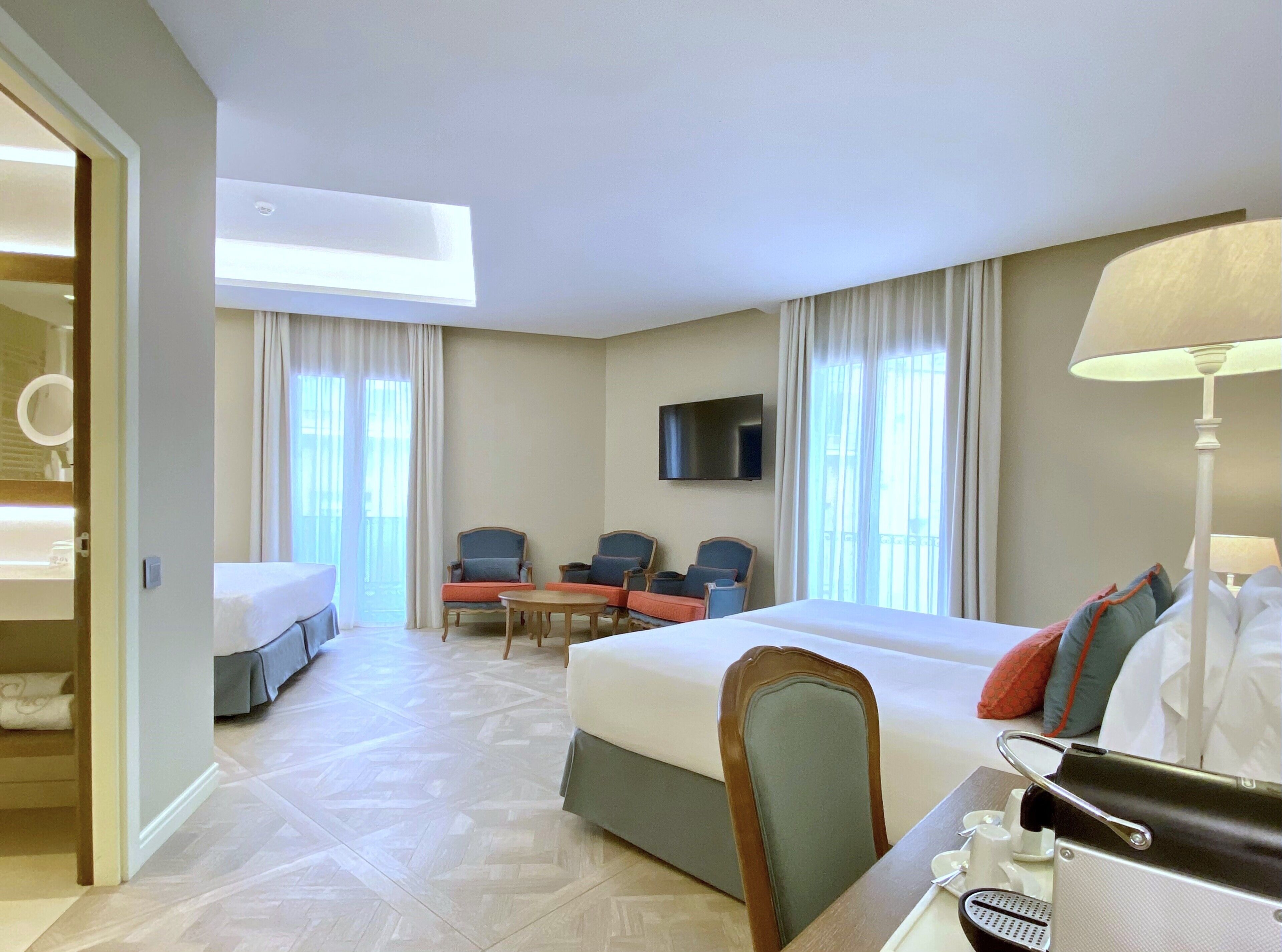 Habitación de hotel con una cama, un escritorio con lámpara, televisión y una zona de estar con sillas.