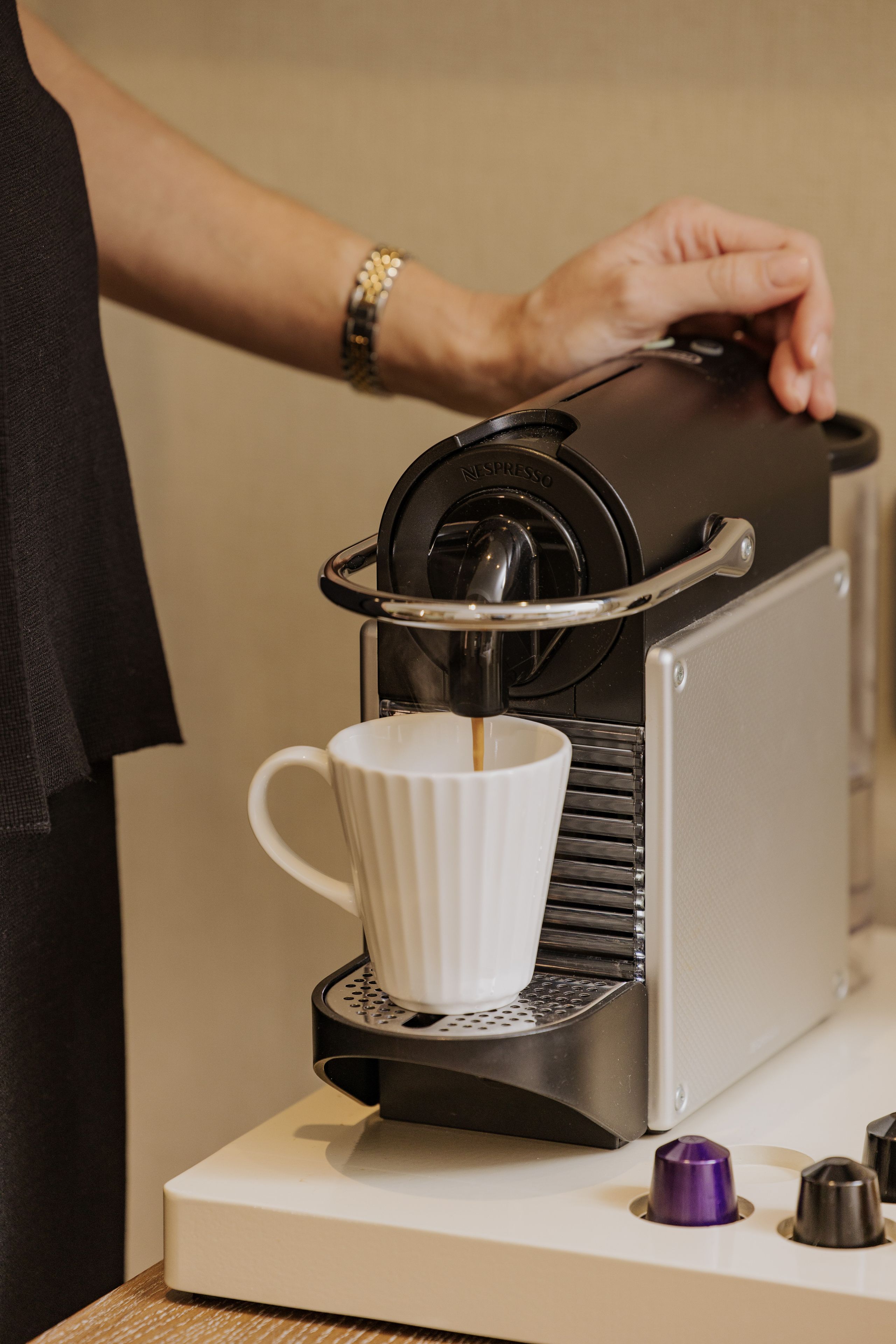 A person operating a coffee machine, with a white cup placed underneath the spout.