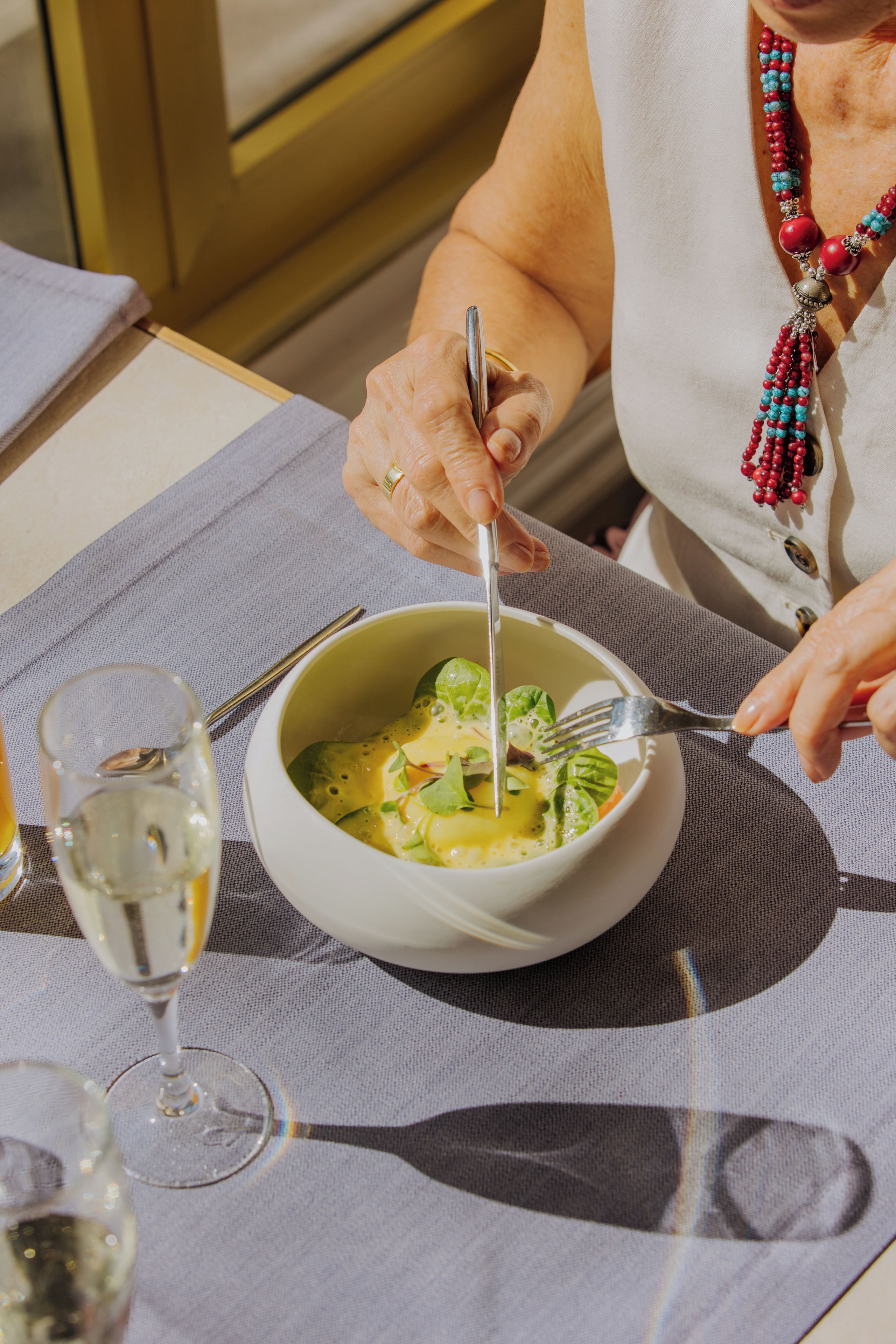A person dining at a table with a bowl of soup and a glass of white wine.