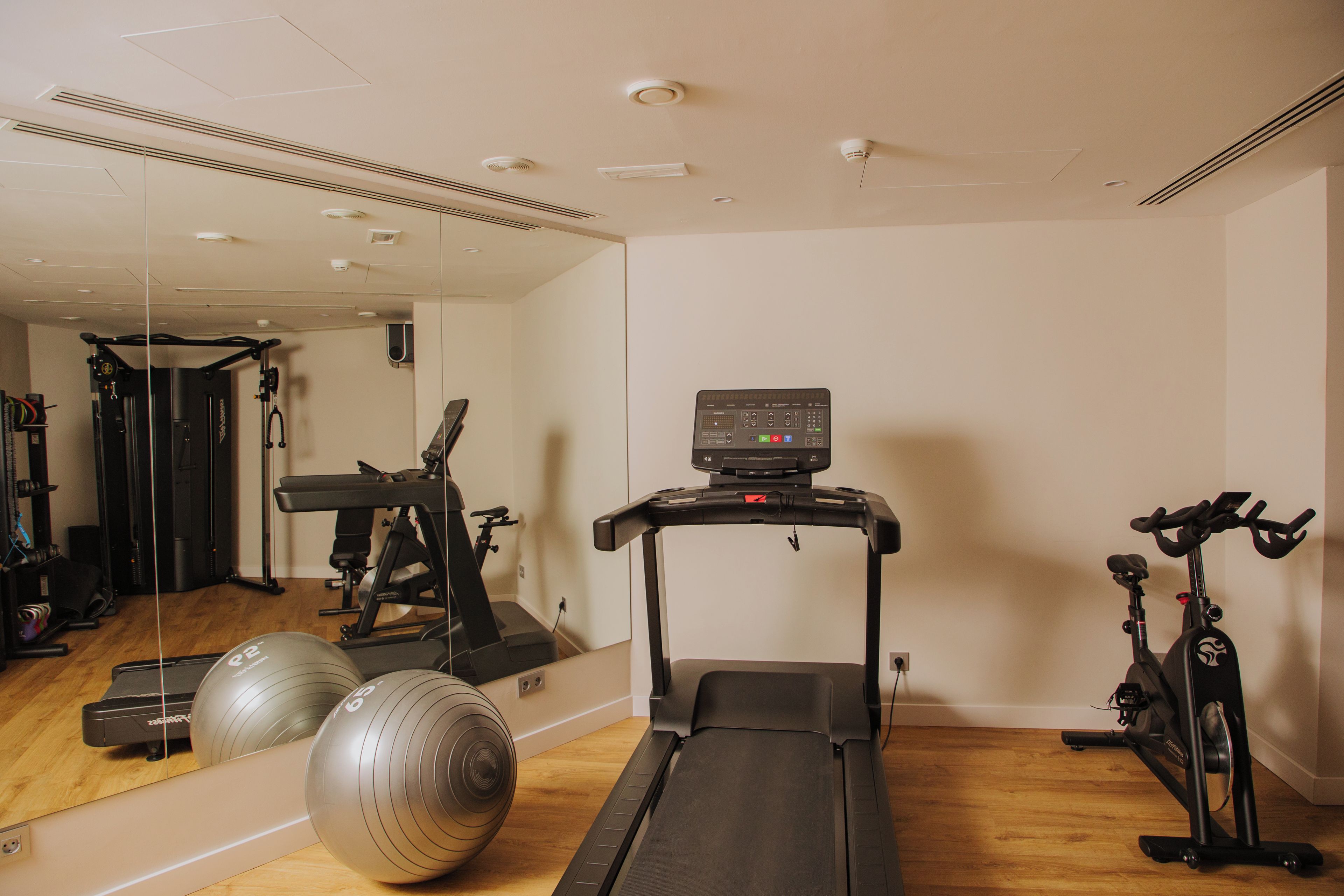 Un gimnasio con equipamiento de ejercicio, incluyendo una cinta de correr, bicicleta estática y pelotas de gimnasia.