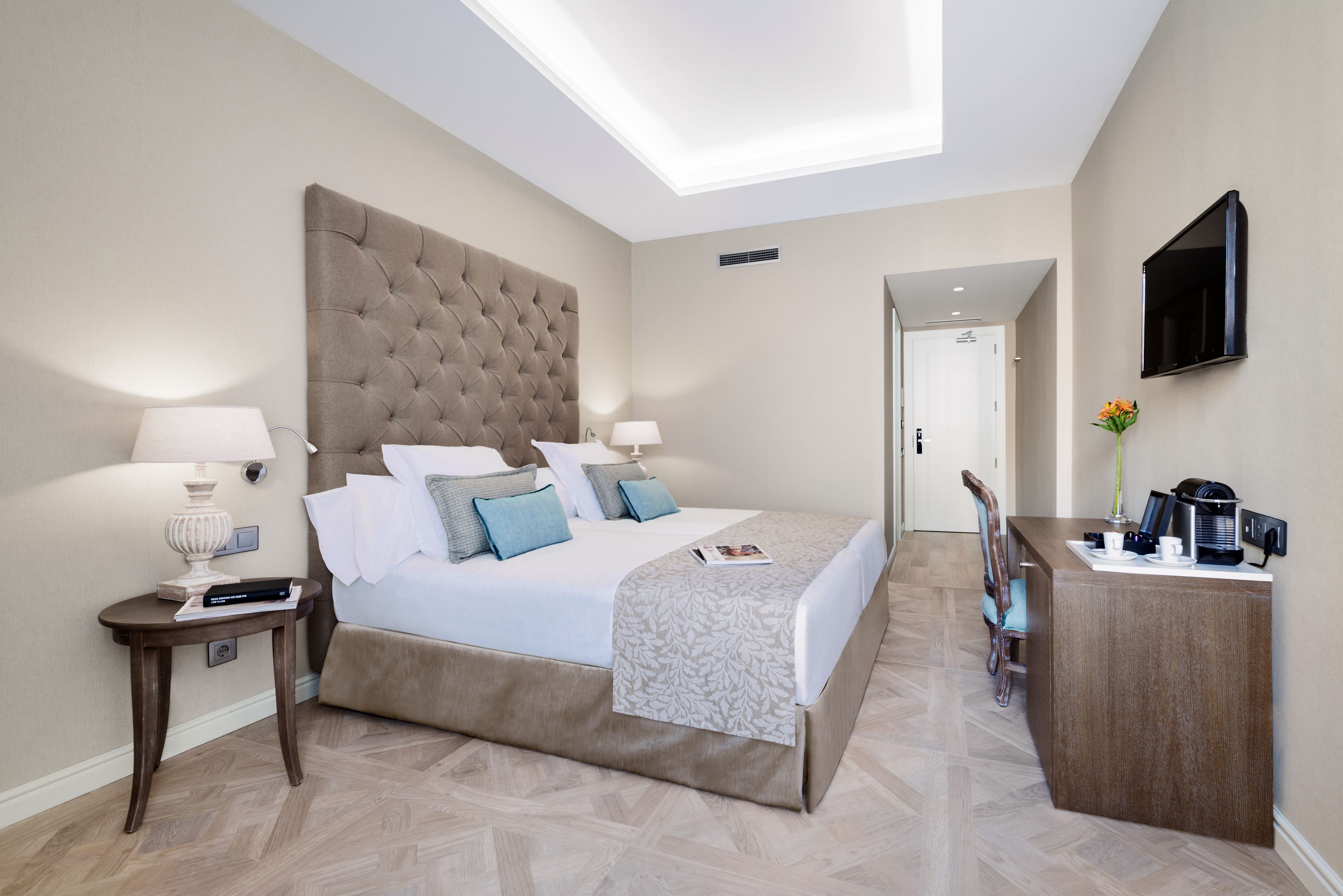 A modern hotel room with a large bed, bedside tables, a desk, and a flat-screen TV.