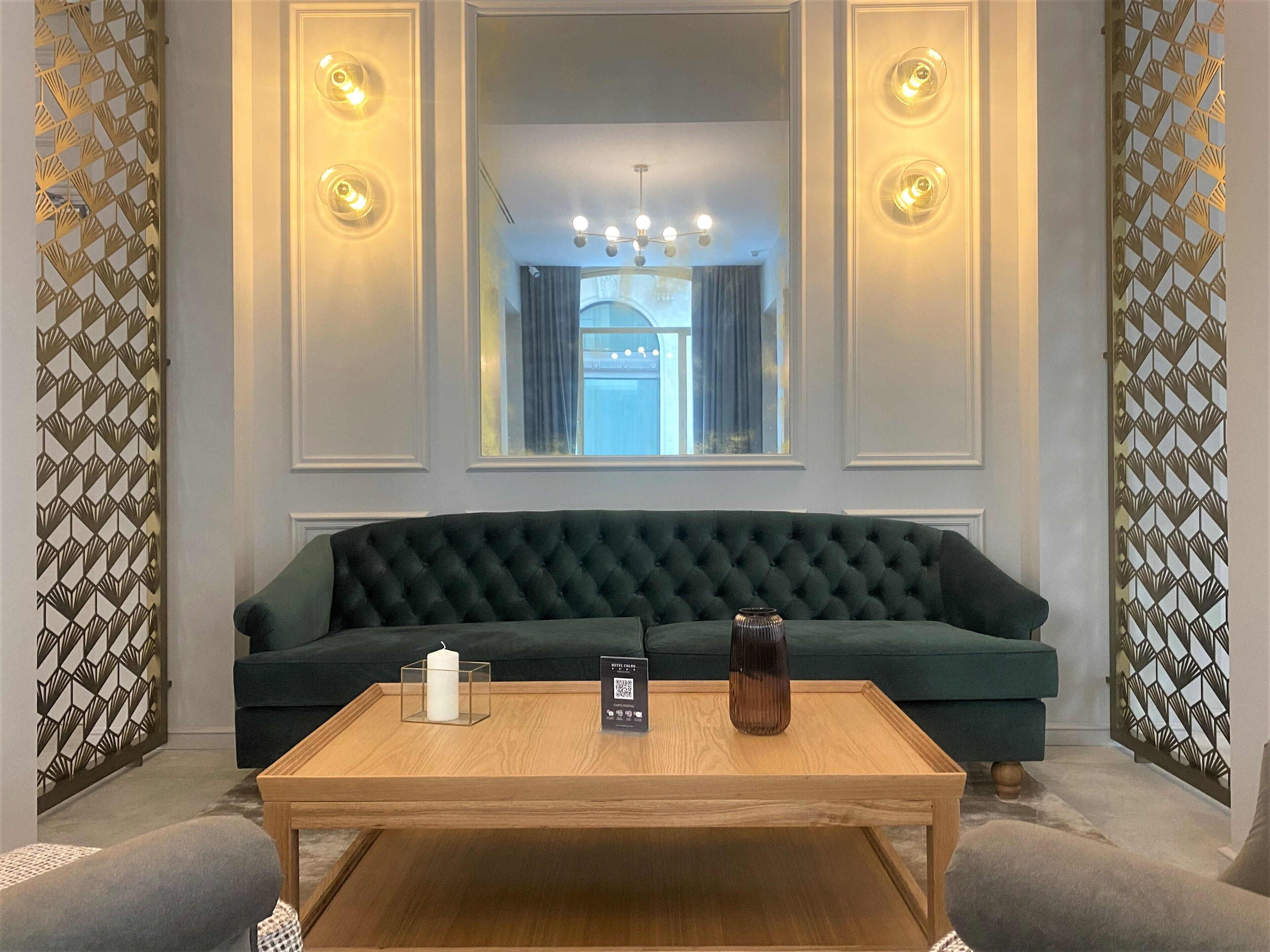 Una habitación con un sofá verde, una mesa de centro de madera y un espejo con apliques de pared.