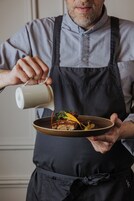 Una persona con delantal oscuro sirve salsa sobre un plato de comida.
