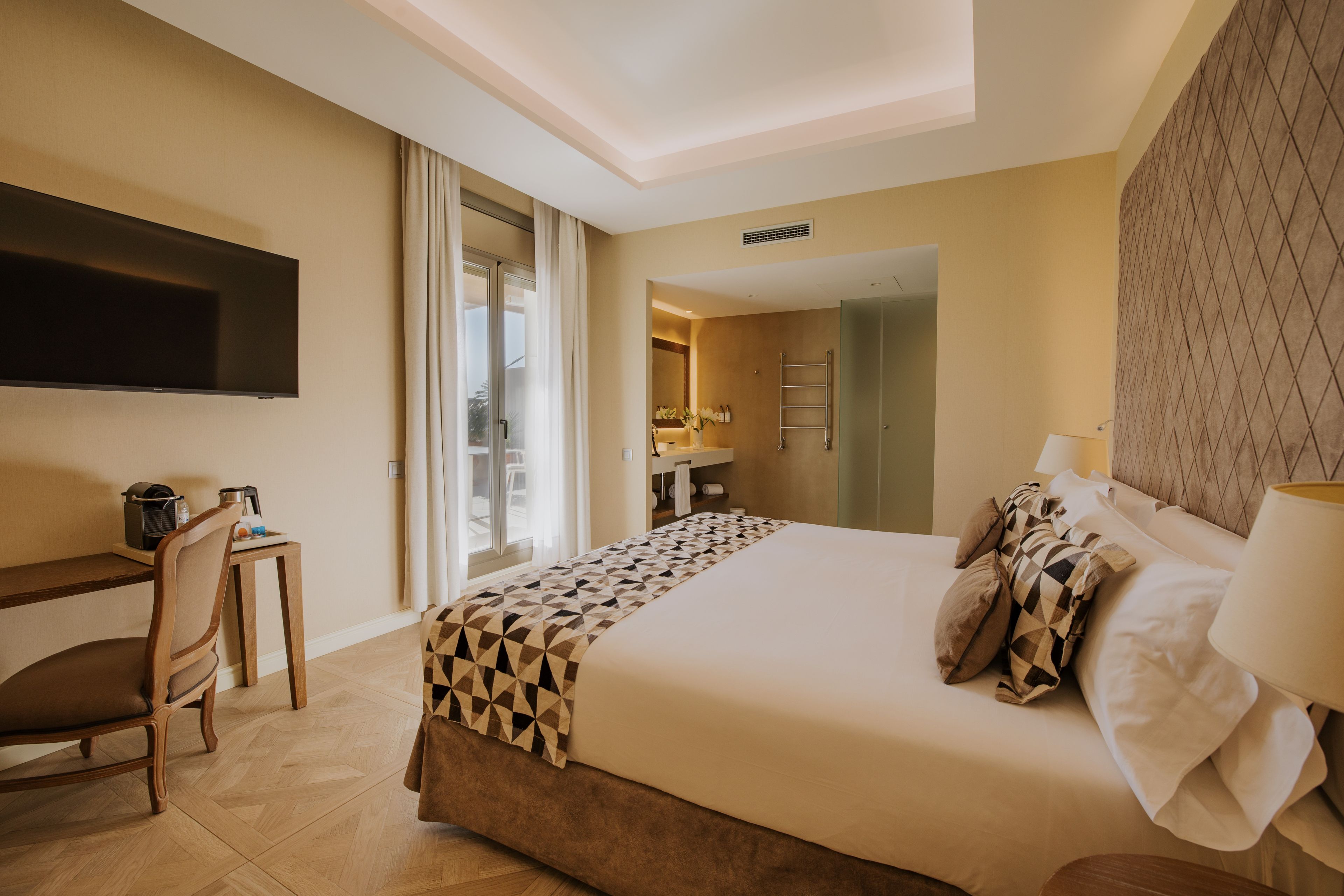A hotel room with a bed, a desk, a chair, a television, and a bathroom visible through an open door.
