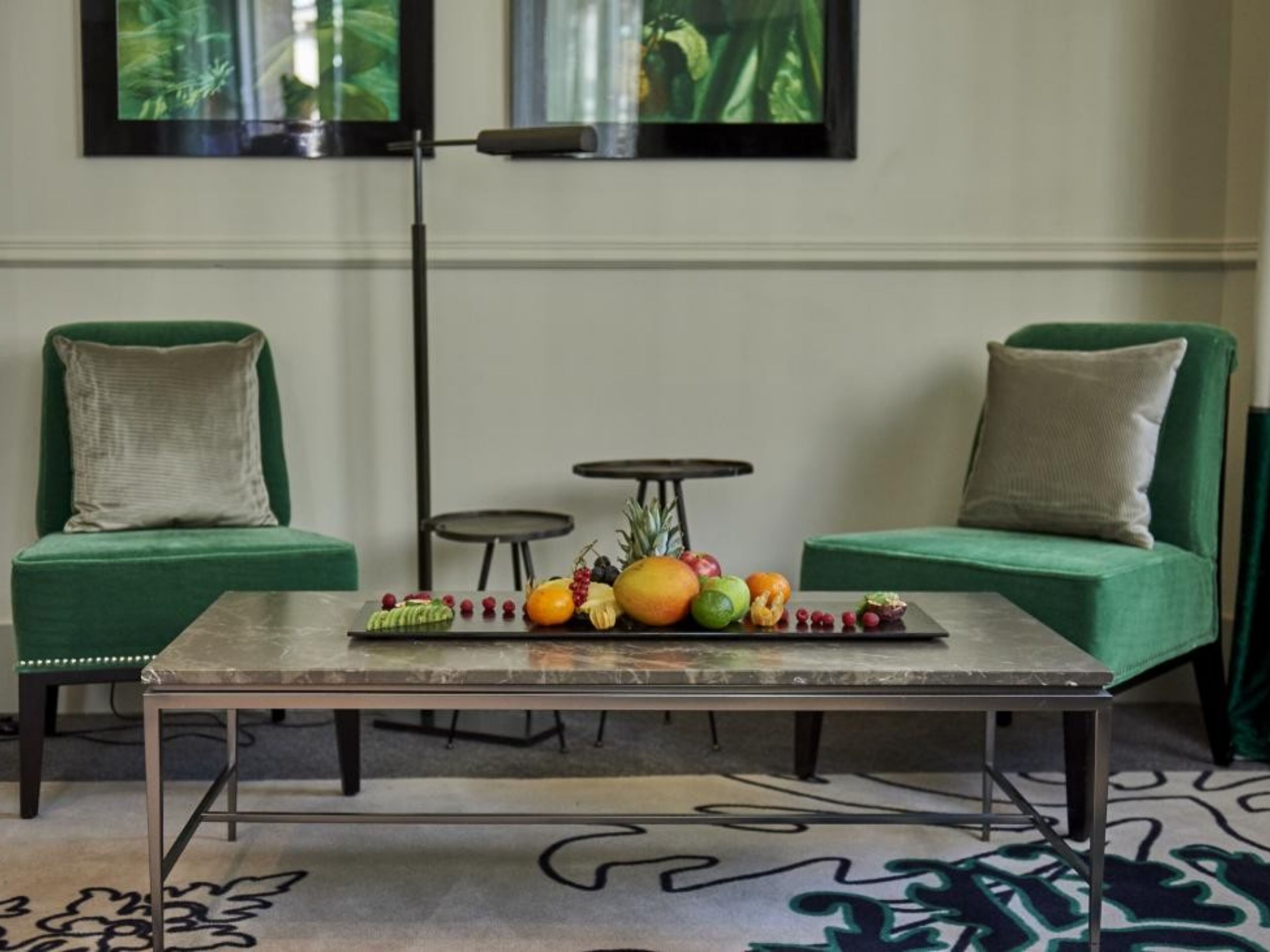 Une pièce comprenant deux canapés verts, une petite table ronde et une table basse sur laquelle sont disposés des fruits.