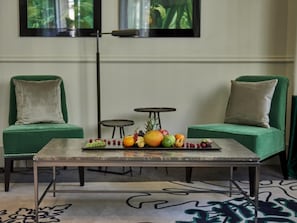 Una habitación con dos sofás tapizados en verde, una mesita redonda y una mesa de centro con fruta.