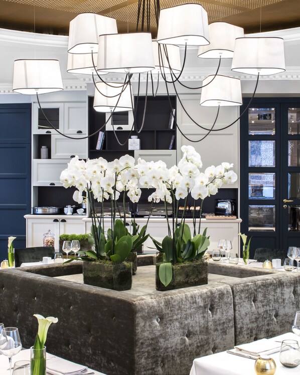 A dining area with white orchids, a modern chandelier, and a dark blue wall. - Hôtel Edouard 7 Paris Opéra (Paris)