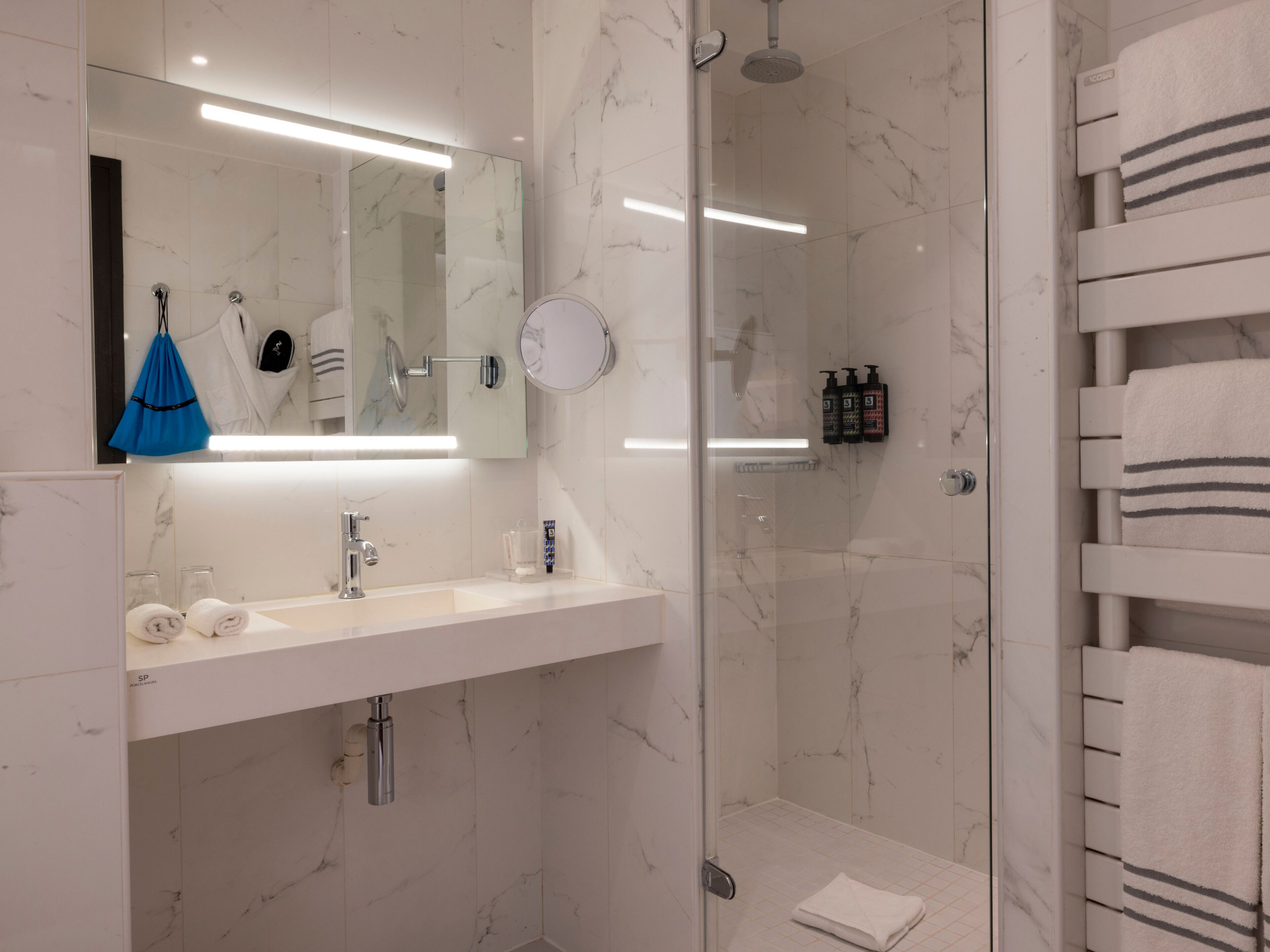 A modern bathroom with a glass shower enclosure, a white sink with a mirror above, and a towel rack with folded towels.