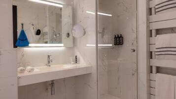 A modern bathroom with a glass shower enclosure, a white sink with a mirror above, and a towel rack with folded towels.