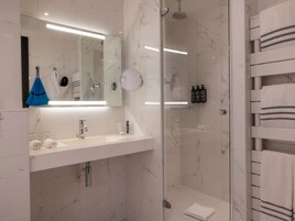 Une salle de bain moderne avec une douche à l’italienne en verre, un lavabo blanc avec un miroir au-dessus et un porte-serviettes avec des serviettes pliées.