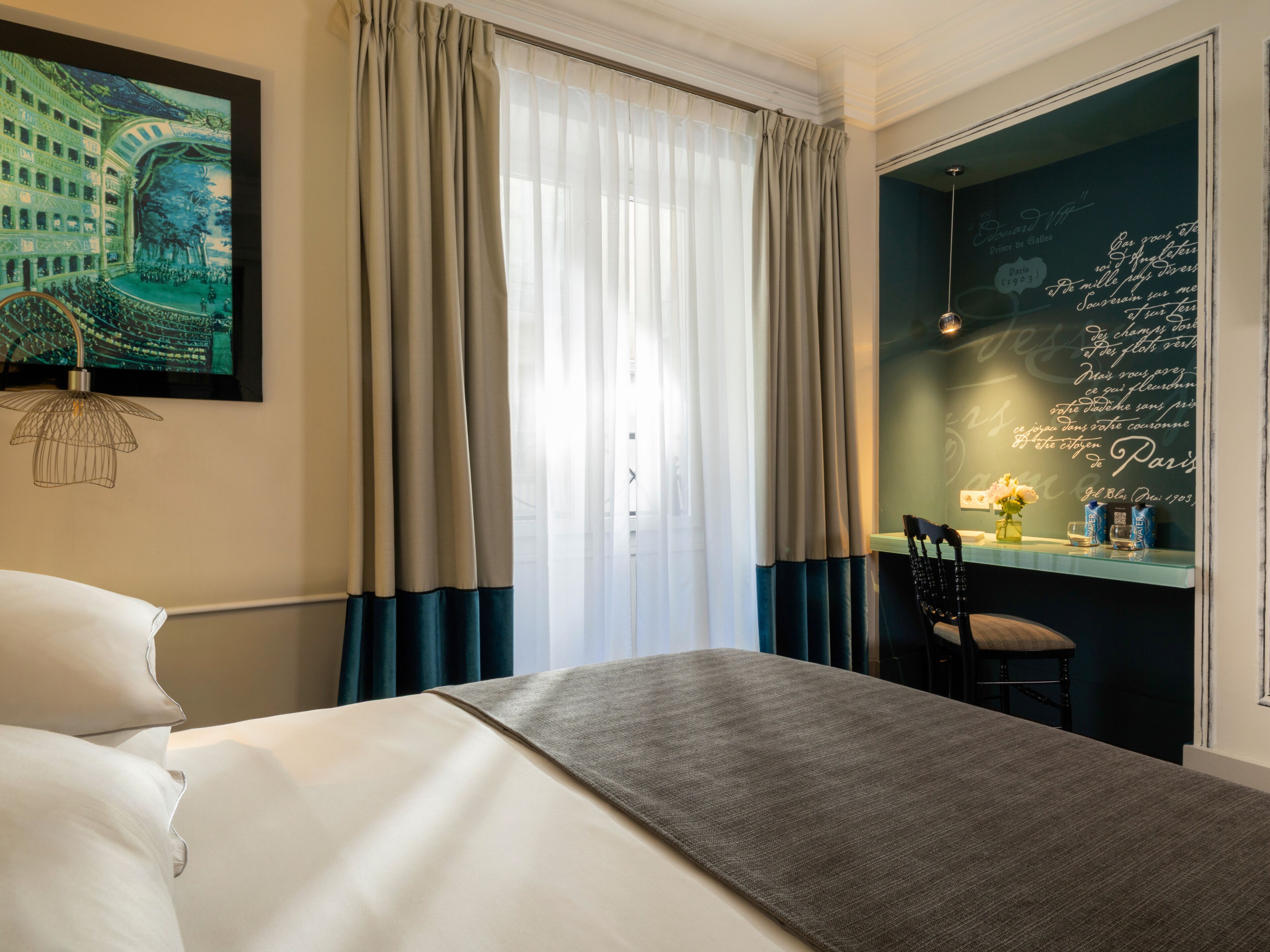A hotel room with a bed, a desk with a chair, a window with curtains, and a wall with writing.