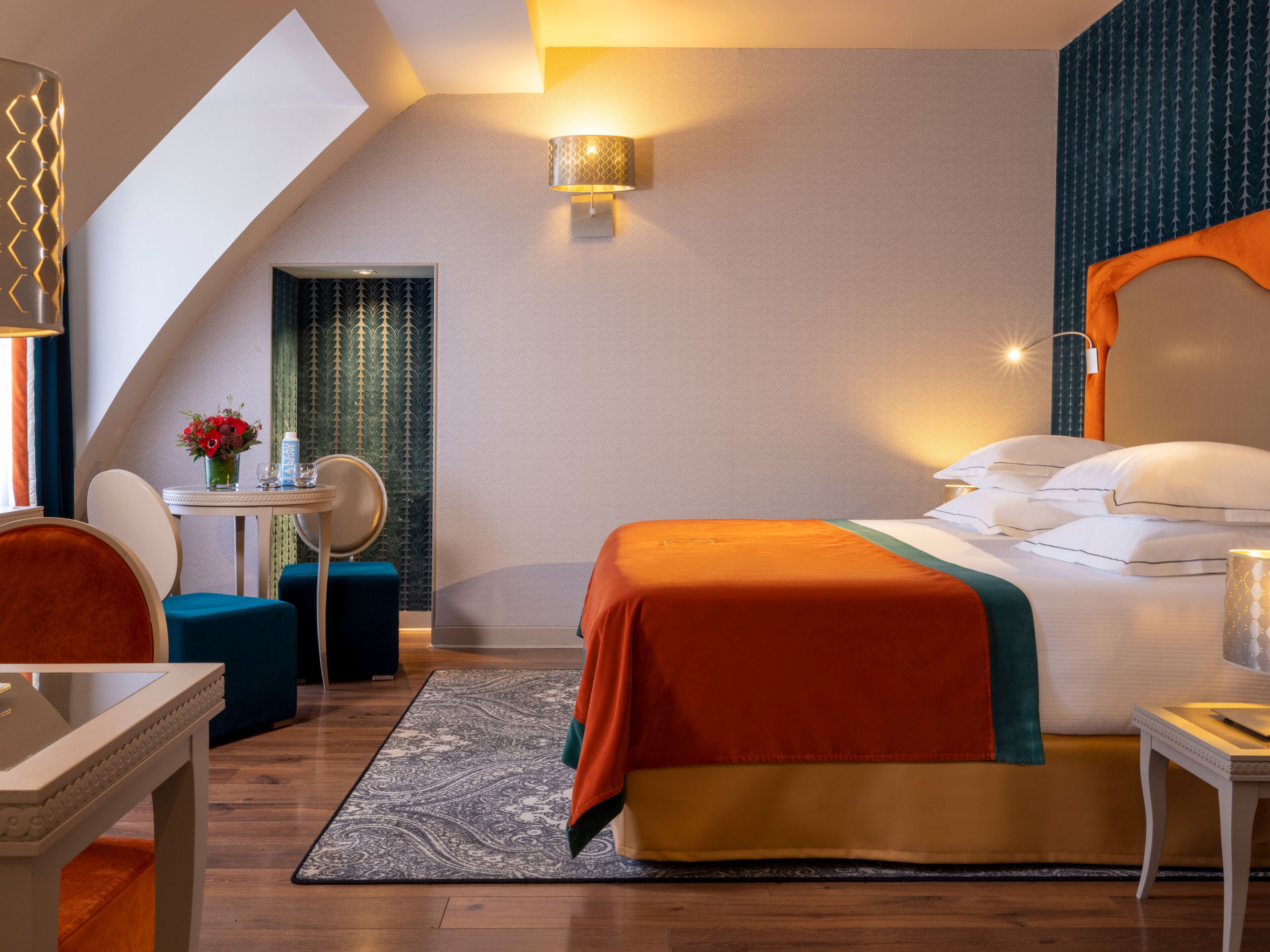 A hotel room with a bed, a desk, a chair, a small table, and a decorative wall.
