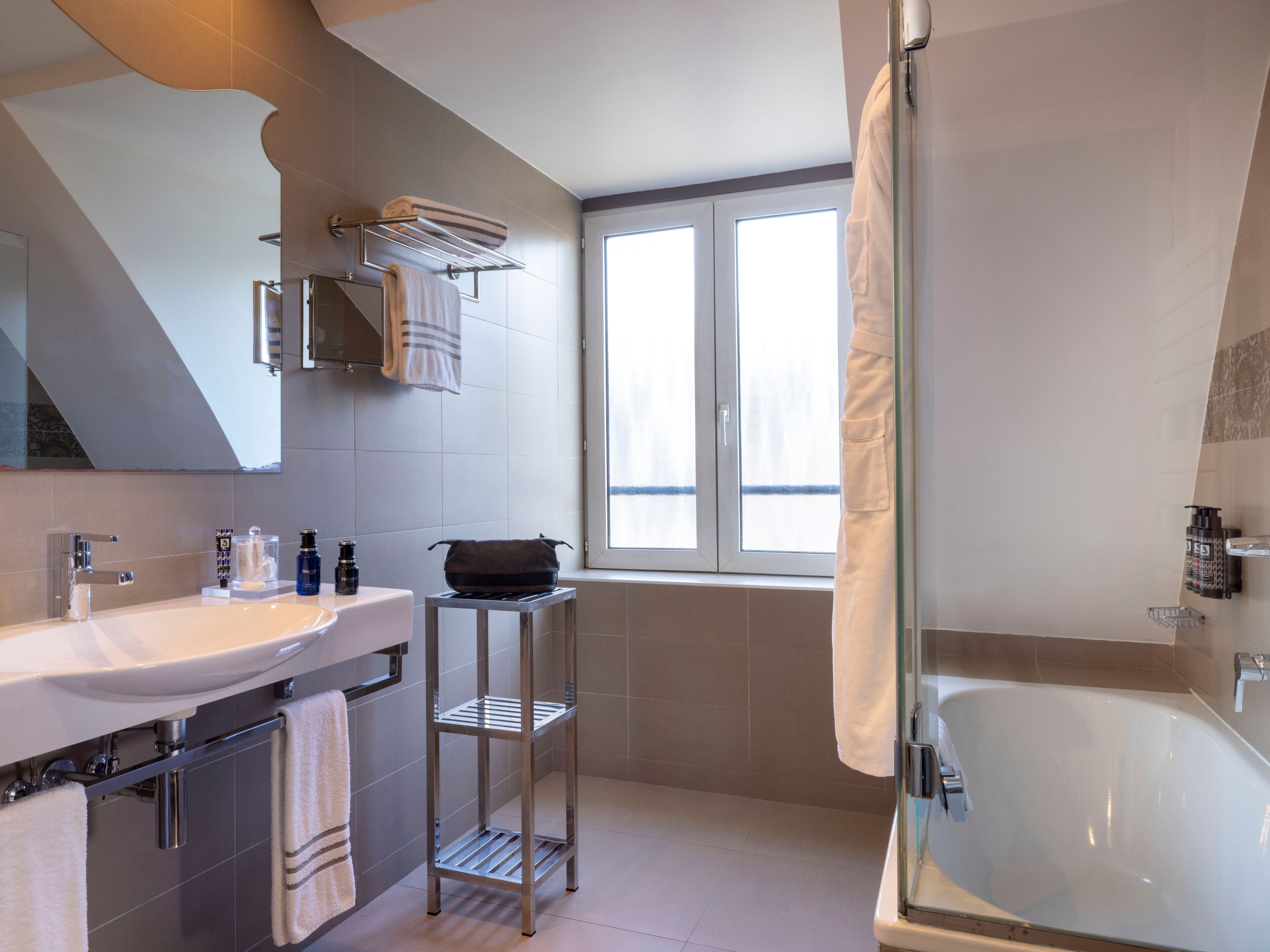 Une salle de bain moderne dotée d’une grande baignoire, d’un double vasque, d’un porte-serviettes et d’une fenêtre laissant entrer la lumière naturelle.