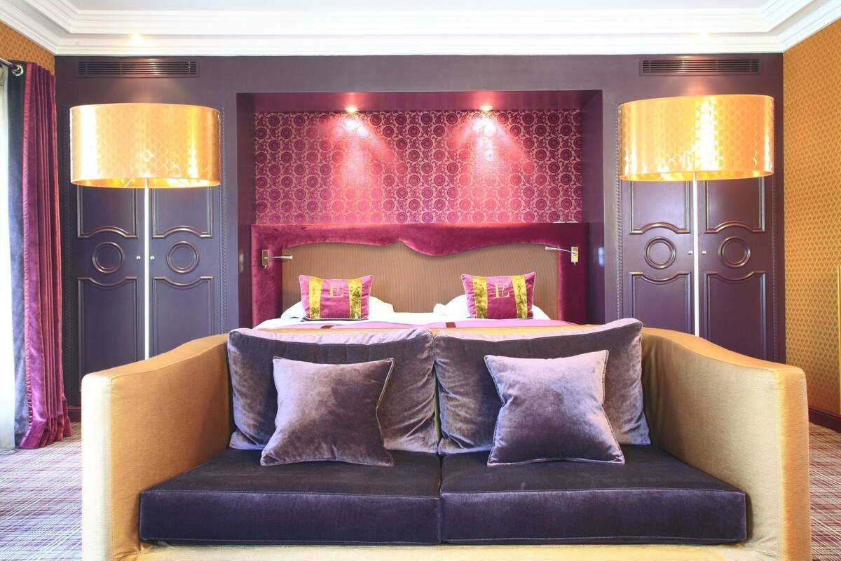 A hotel room with a bed, two bedside lamps, a sofa, and a patterned headboard.