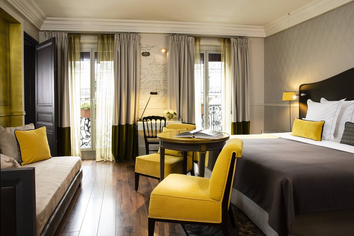 A hotel room with a bed, a sofa, a dining table with chairs, and a balcony view.