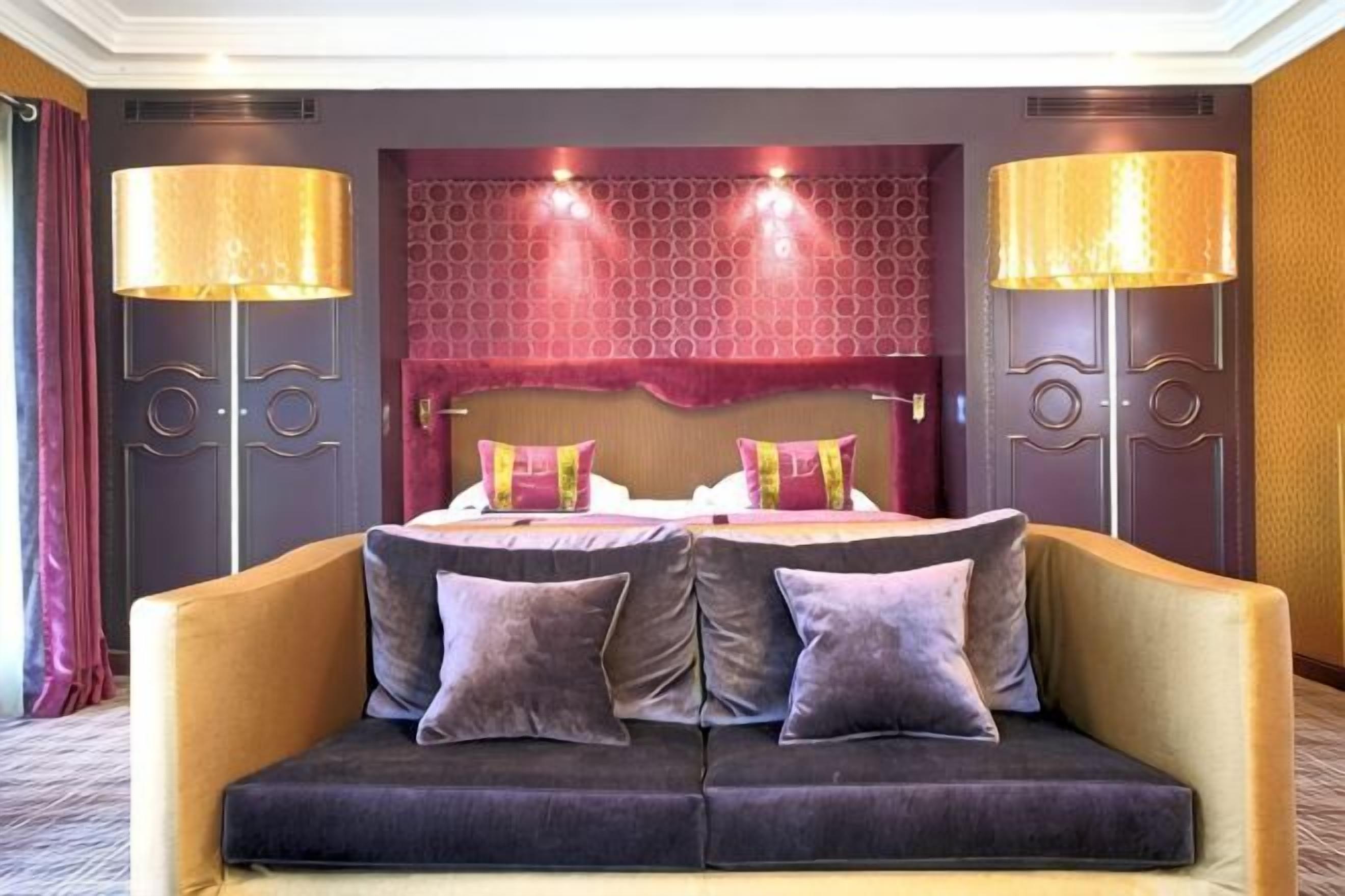 Habitación de hotel con cama doble, dos lámparas de noche, sofá con cojines y cabecera estampada.