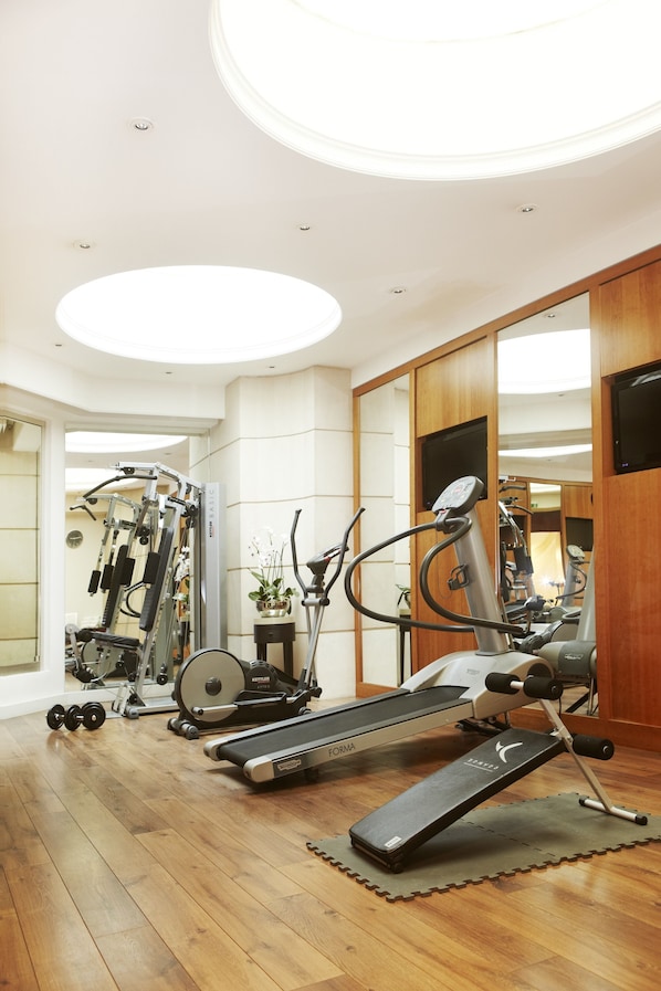 A home gym with a treadmill, elliptical, and weight machines. - Hôtel Edouard 7 Paris Opéra (Paris)
