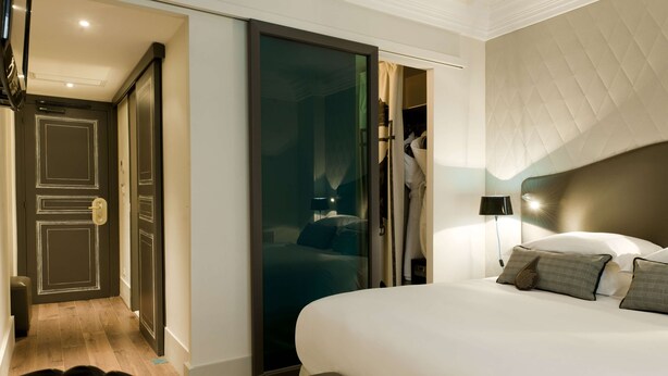A hotel room with a large bed, a wardrobe, a mirror, and a door leading to another room. - Hôtel Edouard 7 Paris Opéra (Paris)
