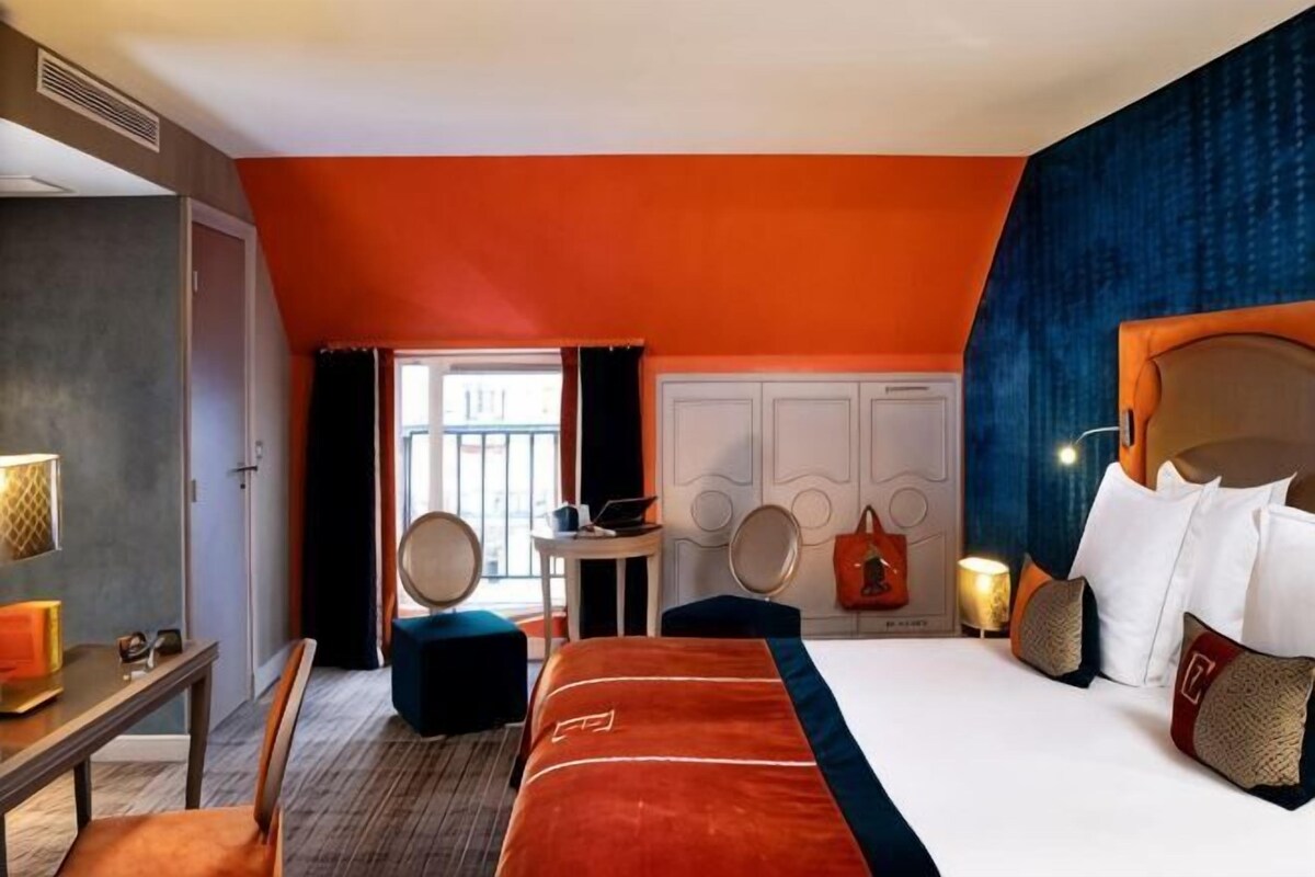 Habitación de hotel con cama, mesitas de noche, escritorio, silla, una mesa redonda y vistas al exterior.
