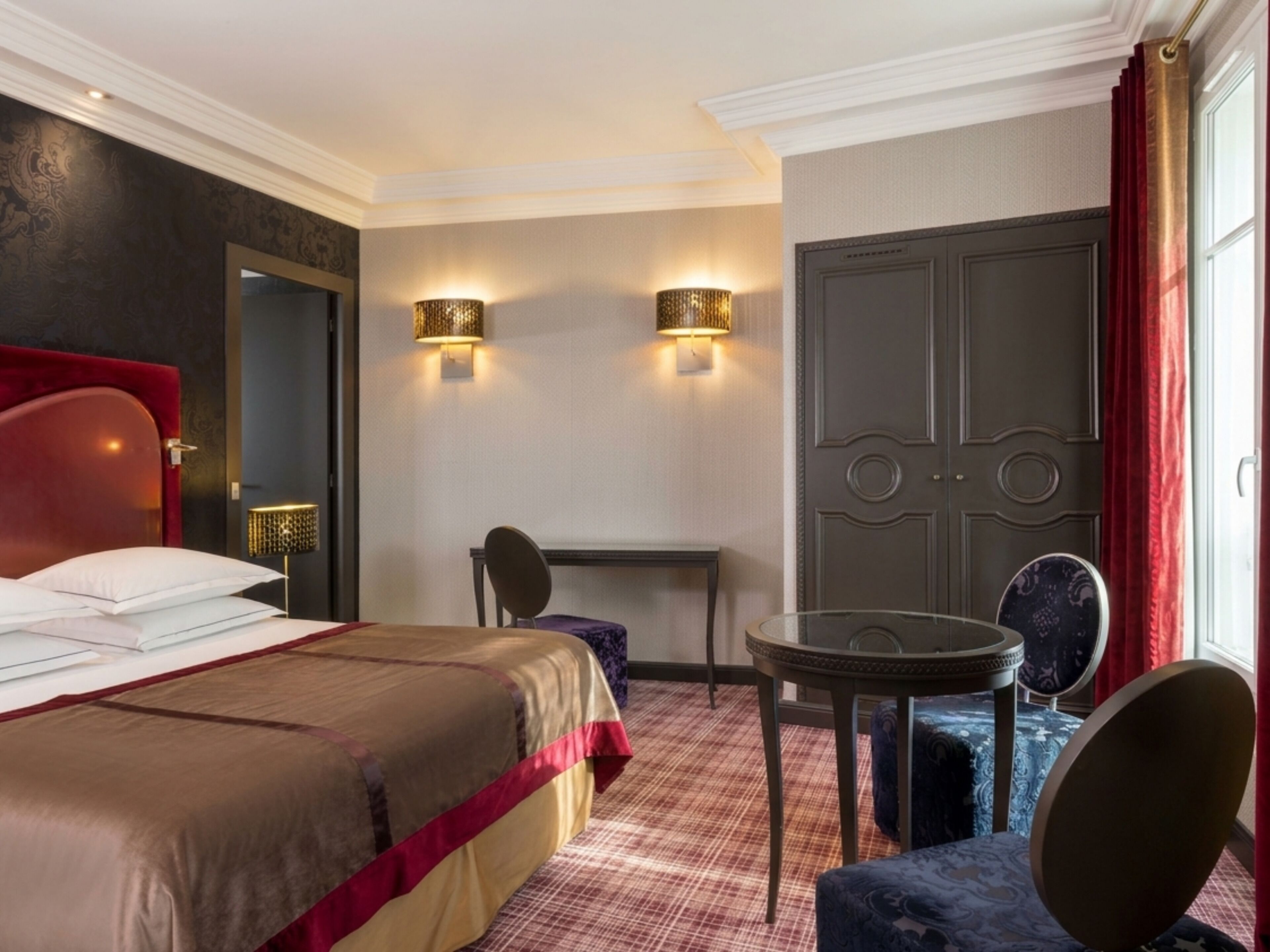 Habitación de hotel con cama, escritorio, silla, mesa redonda y puerta.