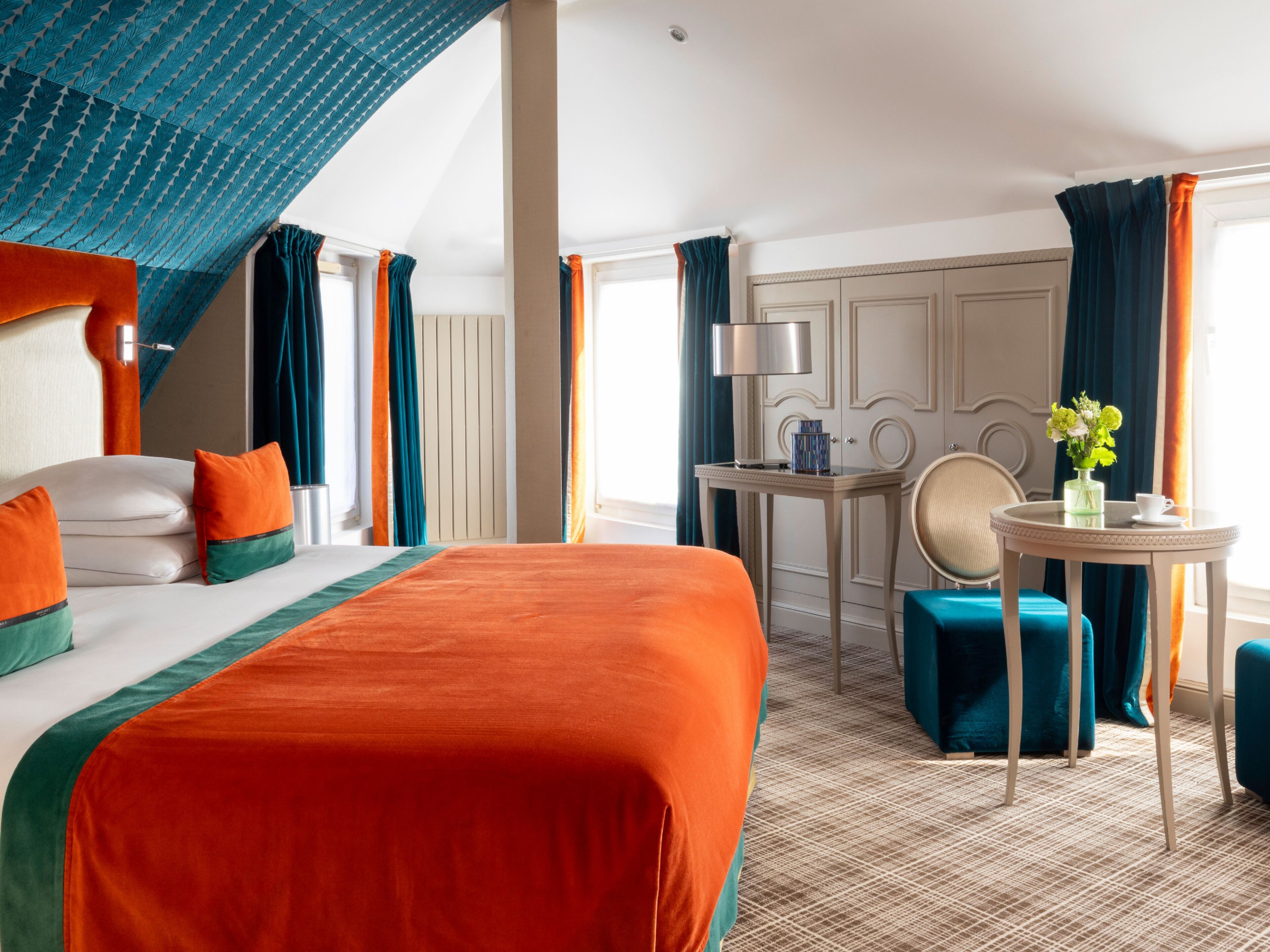 A hotel room with a large bed, a desk, a chair, and a small table with a vase of flowers.