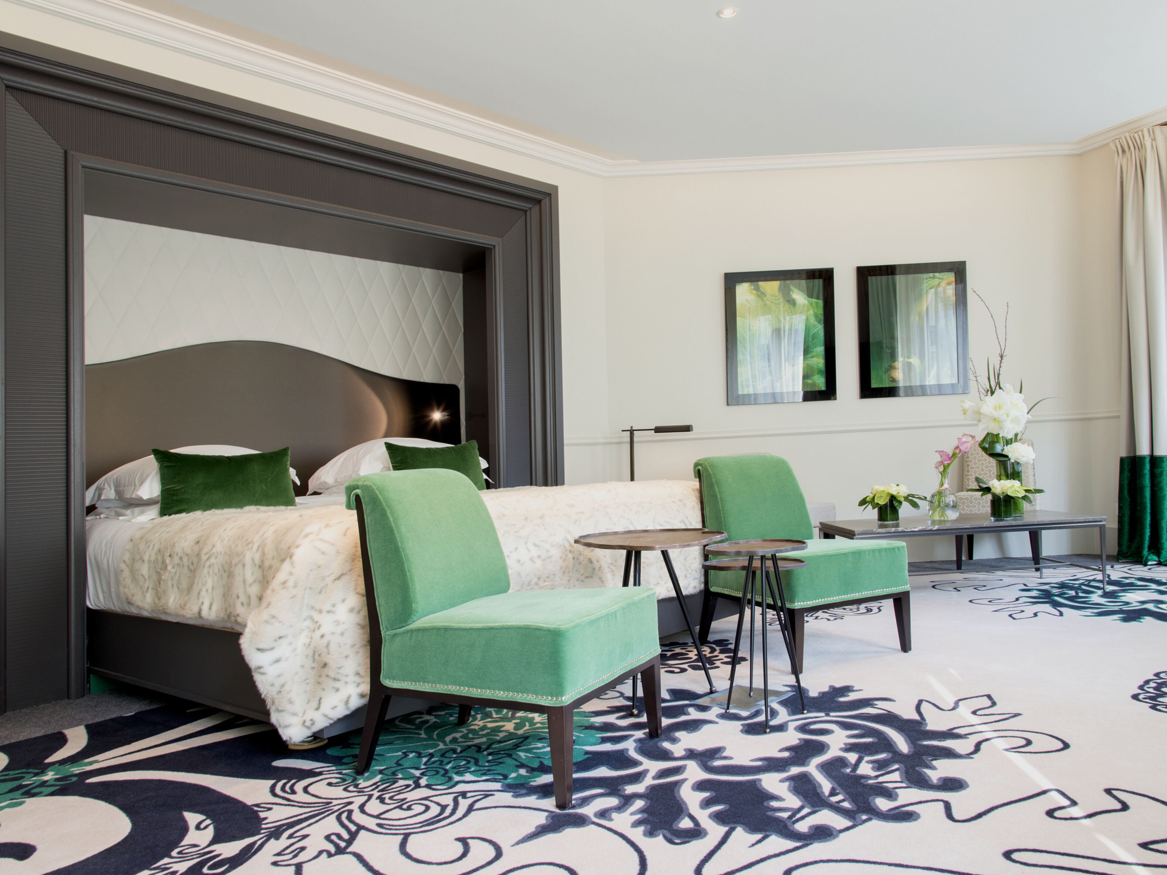 Una camera d'albergo con un letto grande, due poltrone verdi, un tavolino e un tappeto decorativo.