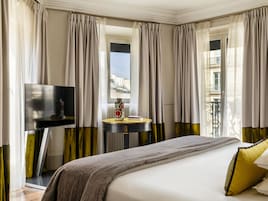 A hotel room with a bed, a TV, a round table with a vase, and curtains.