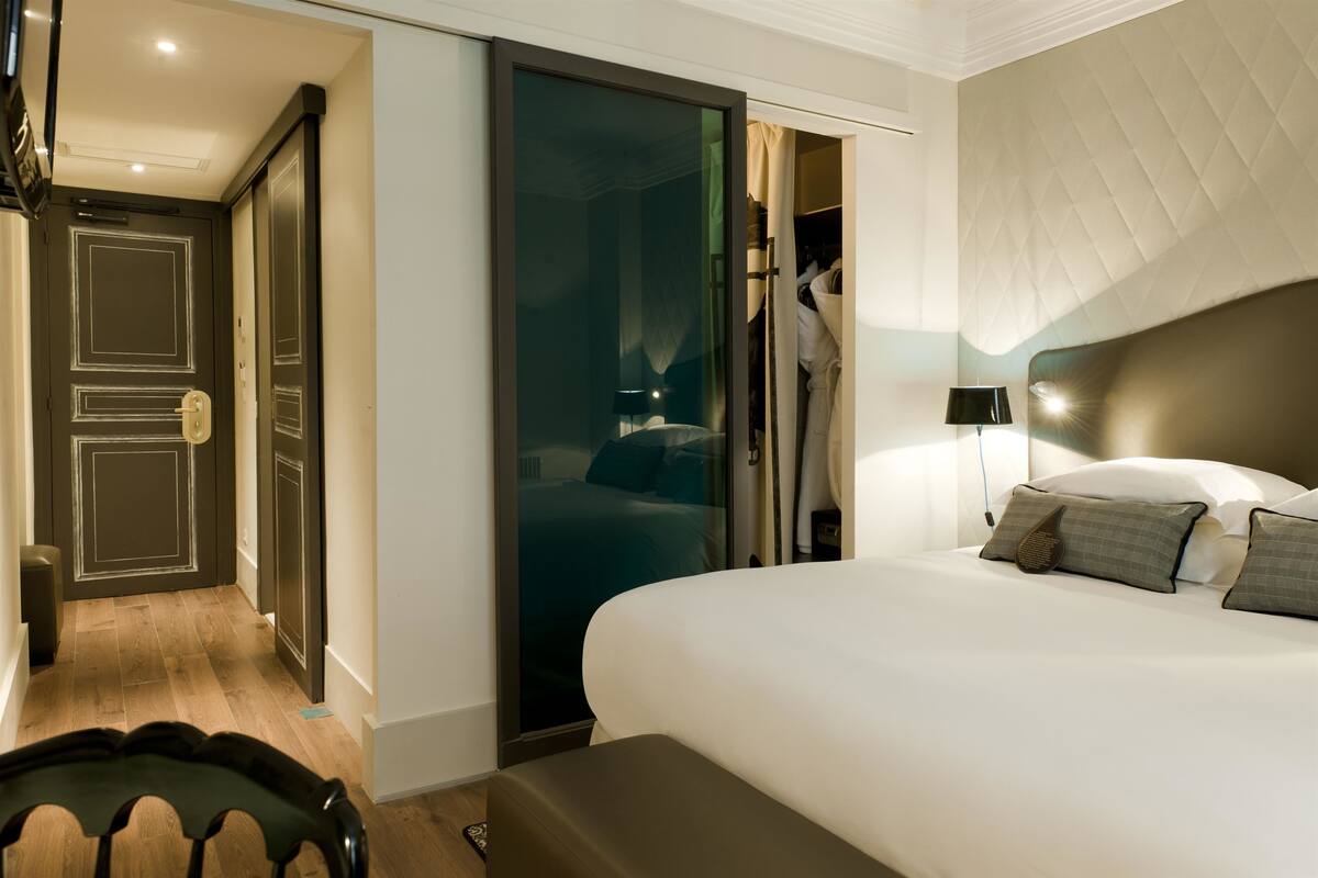 A hotel room with a bed, a chair, a wardrobe, and a door.