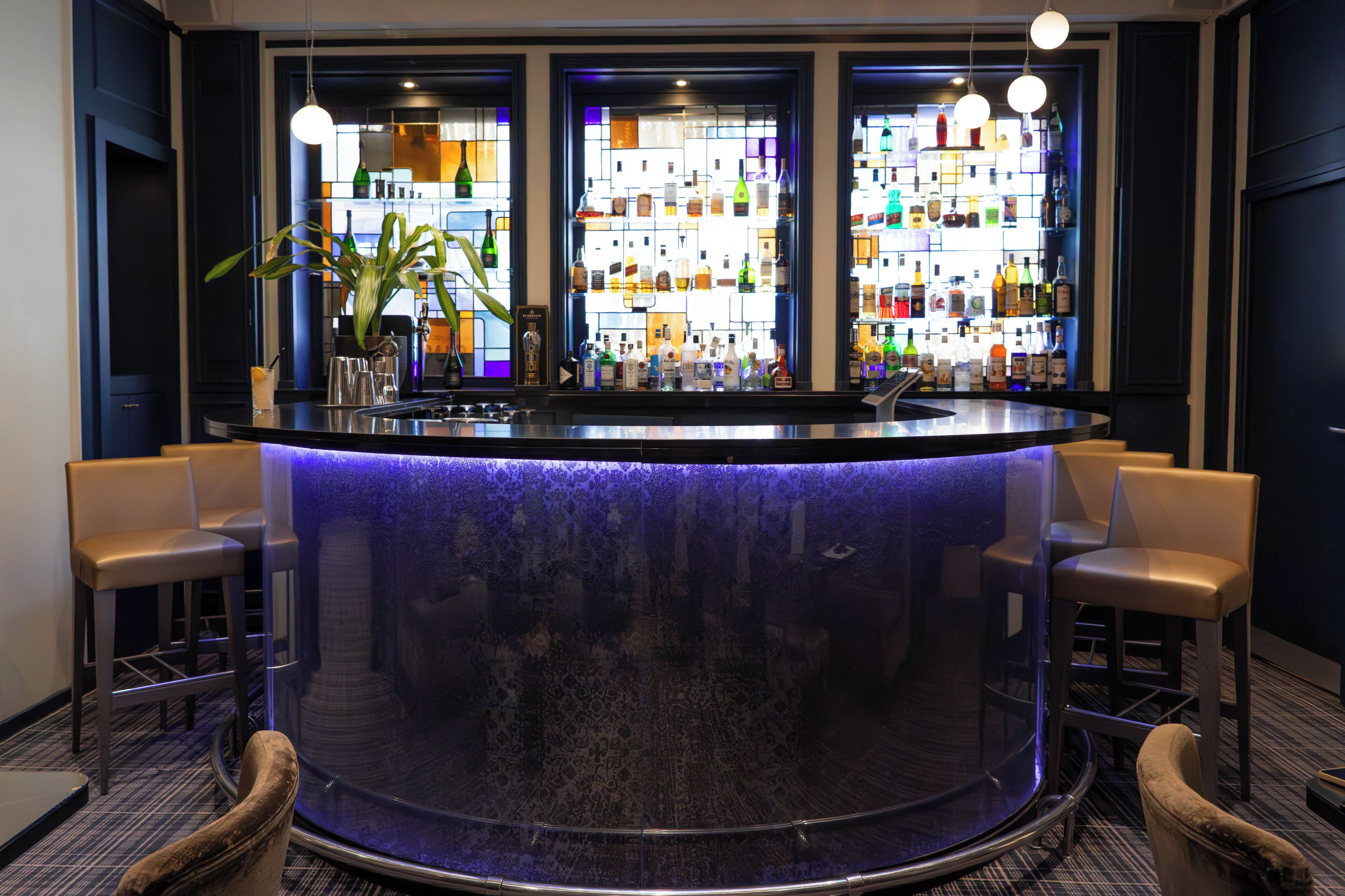 Un espace bar avec un comptoir central, des tabourets et un assortiment de bouteilles.