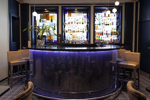 Zona de bar con mostrador central, taburetes y una variedad de botellas.
