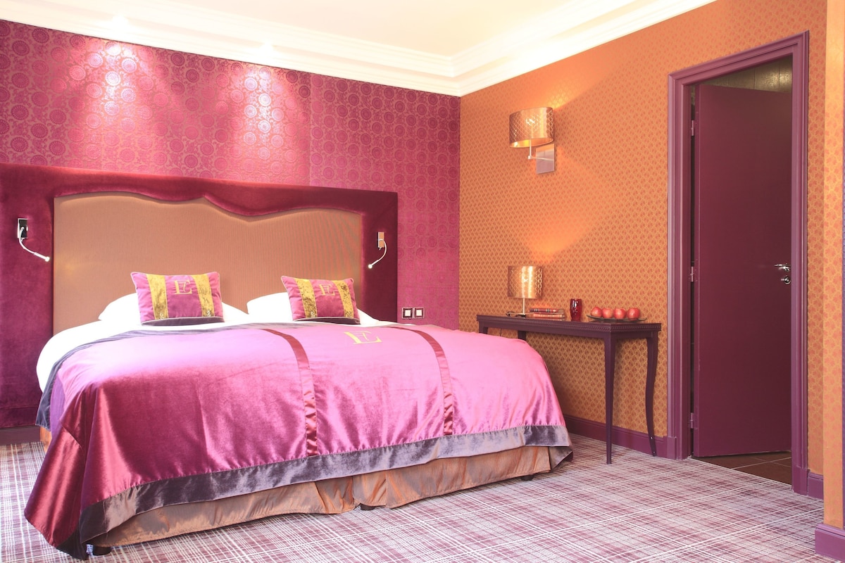 Una habitación de hotel con una cama grande, una mesita de noche, una lámpara y una puerta.