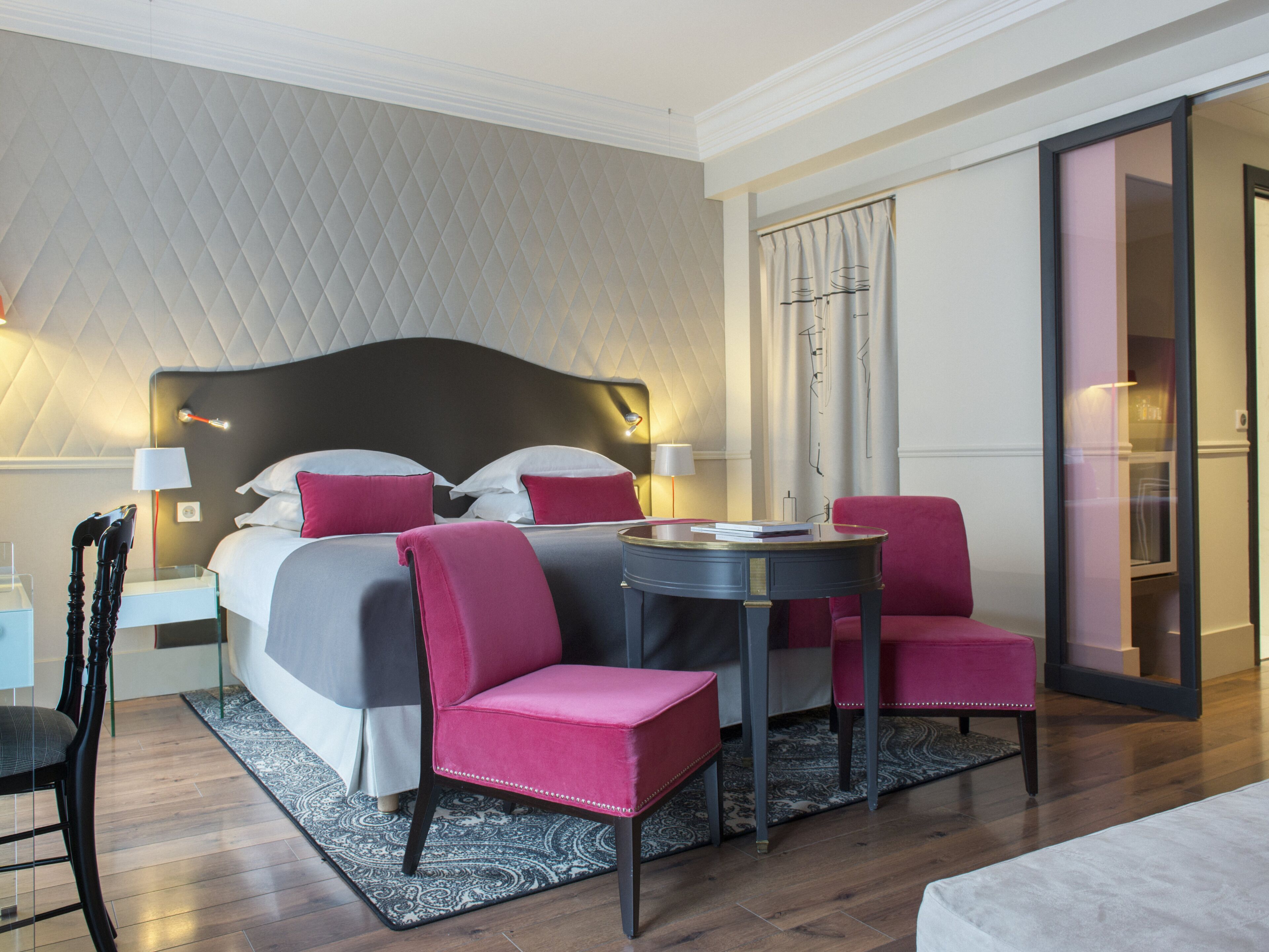 Una habitación de hotel con cama, dos sillas, una mesa y una mesita de noche con lámparas.