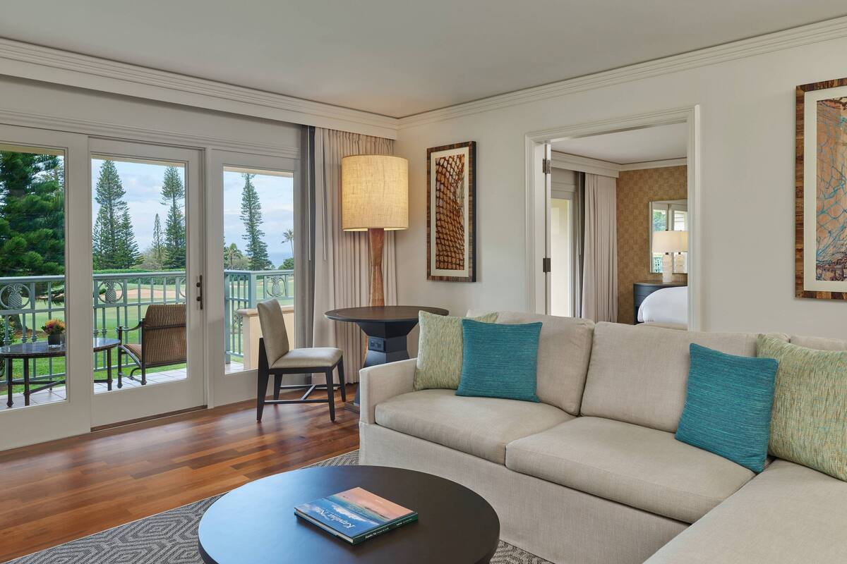 A modern living room with a beige sofa, teal cushions, a round coffee table, and a view of a patio with outdoor furniture.