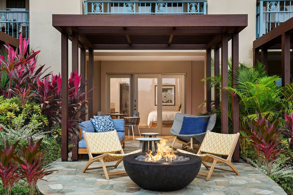 A covered outdoor seating area with a fire pit, wicker chairs, and a view of the interior.
