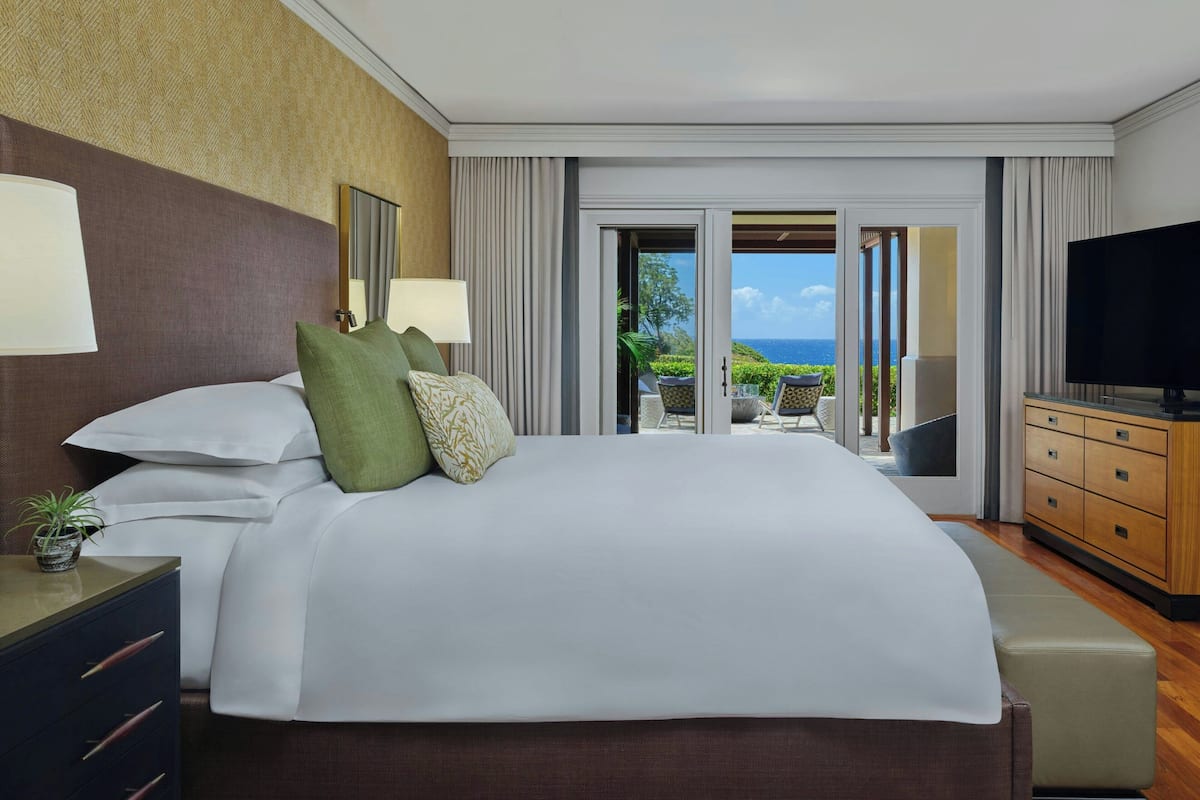 A hotel room with a large bed, a TV, a dresser, and a balcony with a view of the ocean.