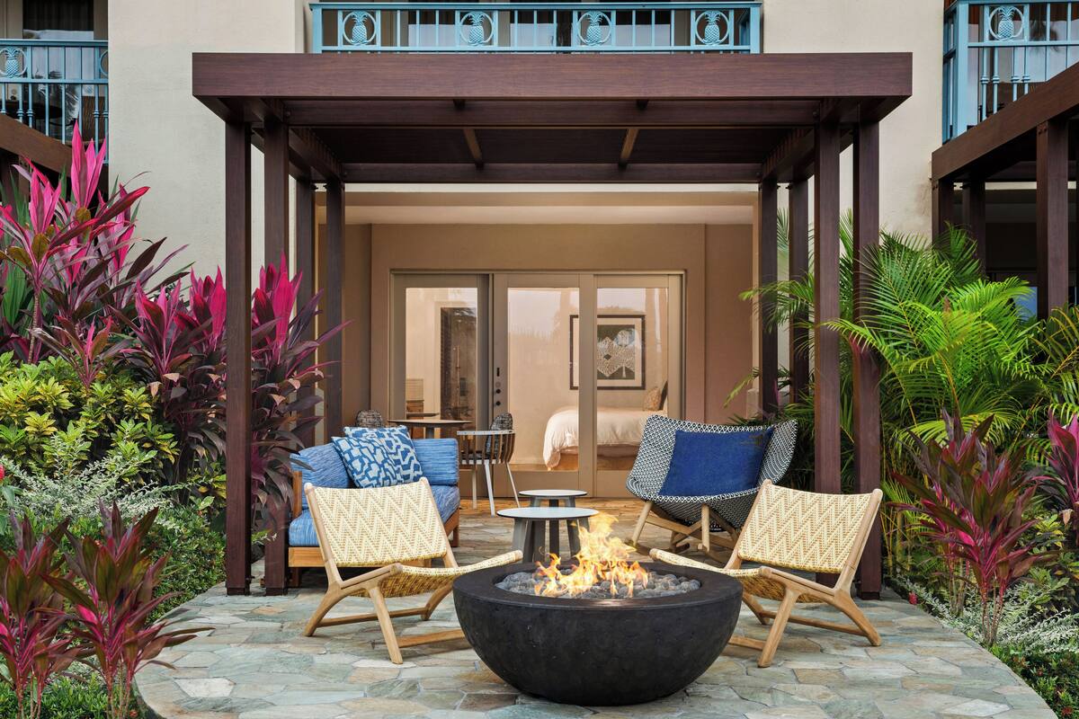 An outdoor seating area with a fire pit, lounge chairs, and a view of the building's interior.