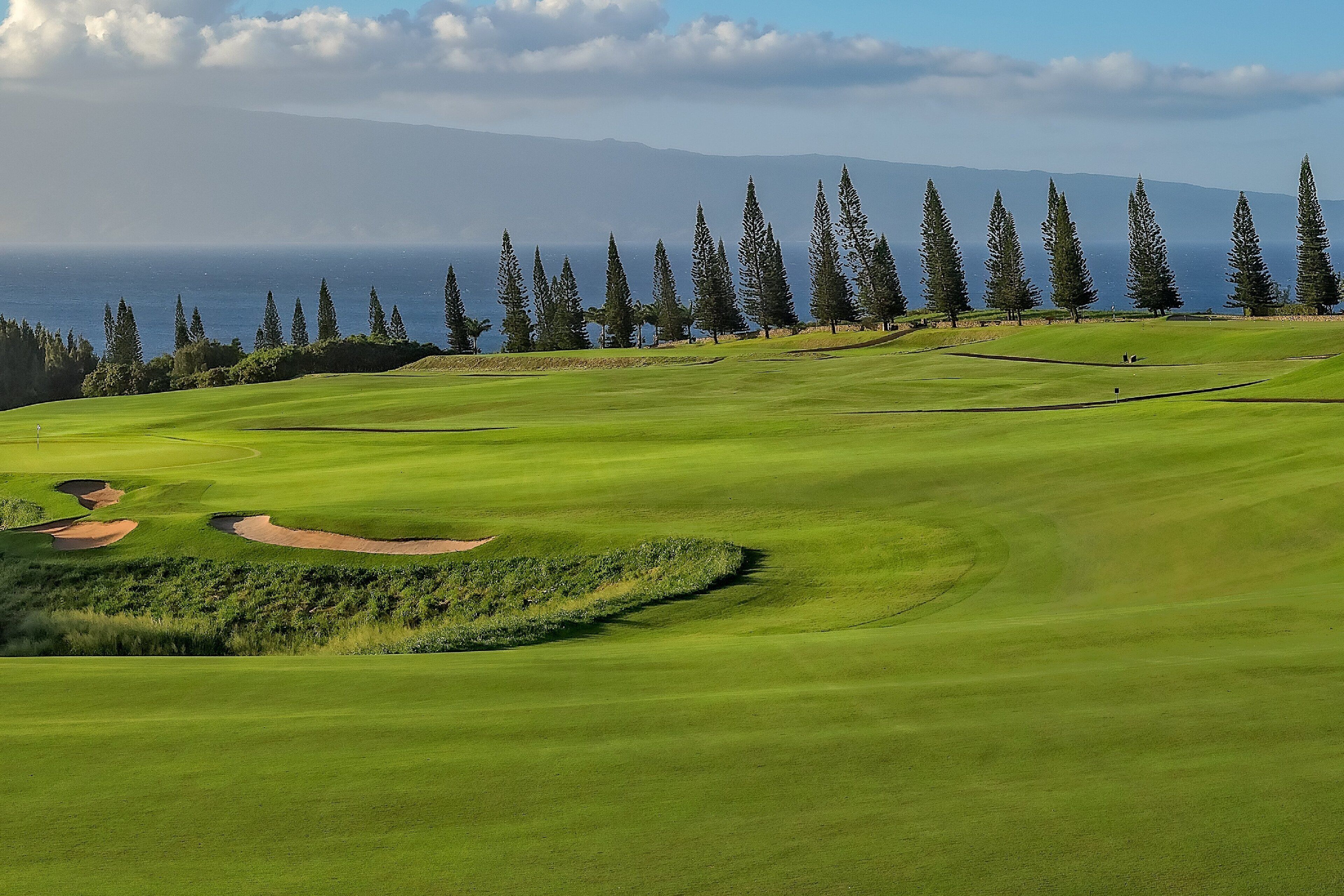 Un parcours de golf offrant une vue sur l’océan et les montagnes en arrière-plan.