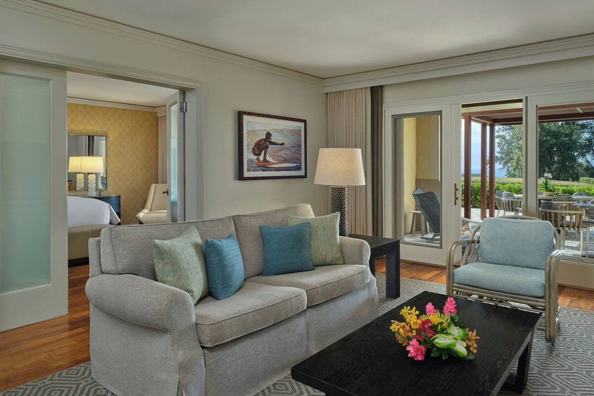 A modern hotel room with a grey sofa, a black coffee table with flowers, and a painting on the wall.