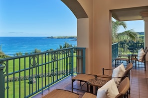 A balcony with a view of the ocean, furnished with wicker chairs and a table.