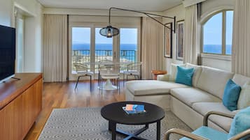 Amplia sala de estar con sofá, una mesa de centro y televisor sobre un mueble de madera. Hay un balcón con vista al océano.