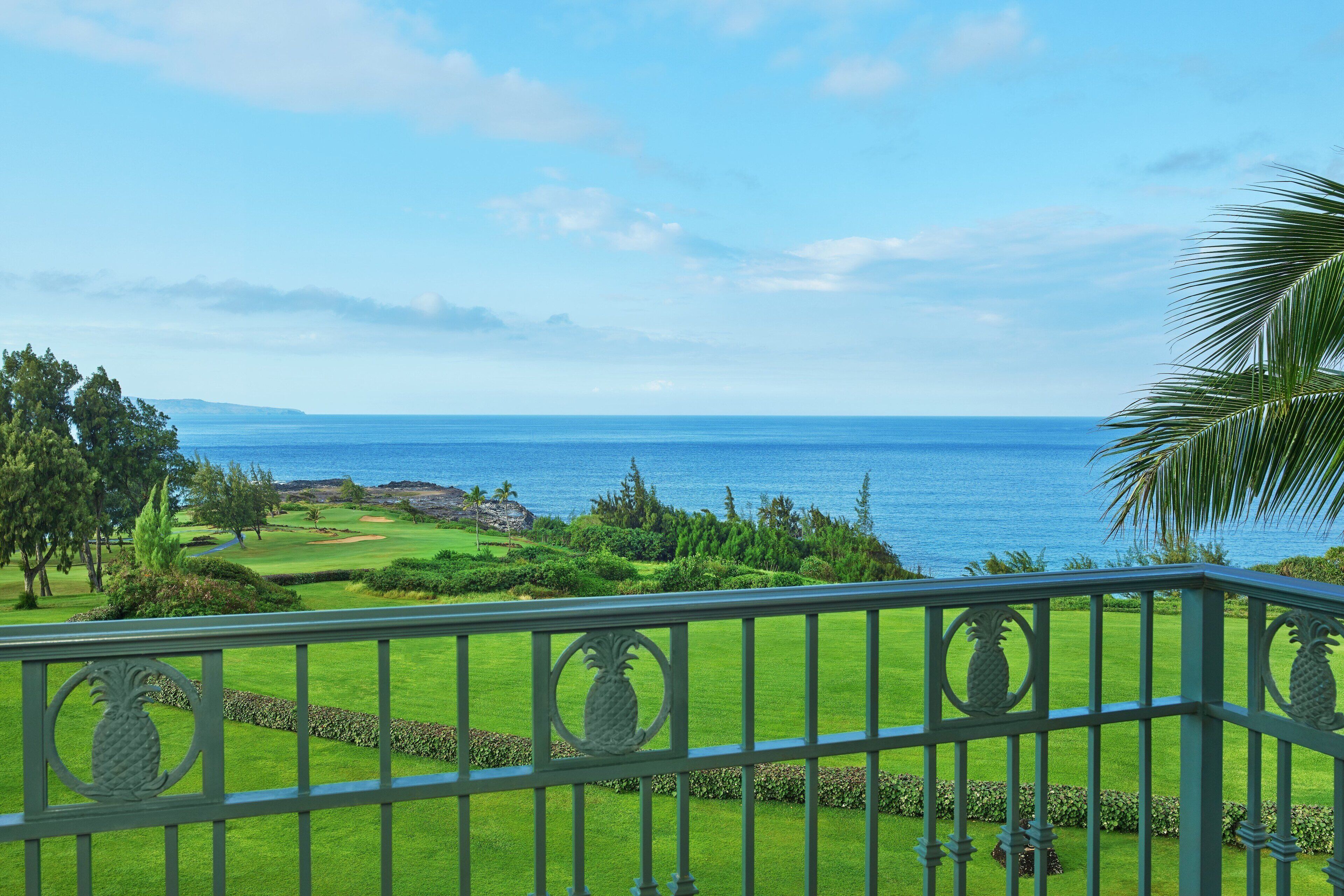 A view from a balcony overlooking a golf course with a clear view of the ocean and distant mountains.