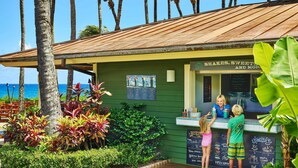 A small outdoor café with a green exterior, a wooden roof, and a view of the ocean.