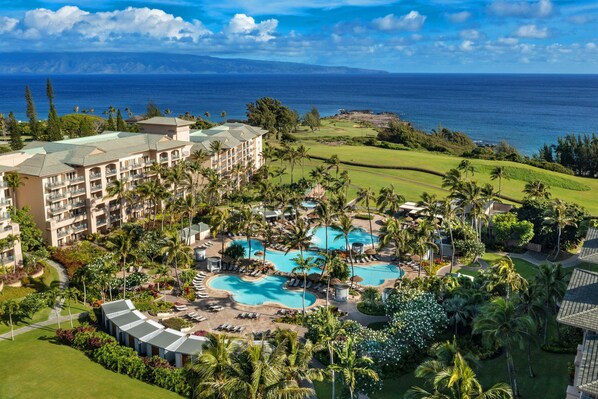 A resort with multiple swimming pools, lush greenery, and a view of the ocean.